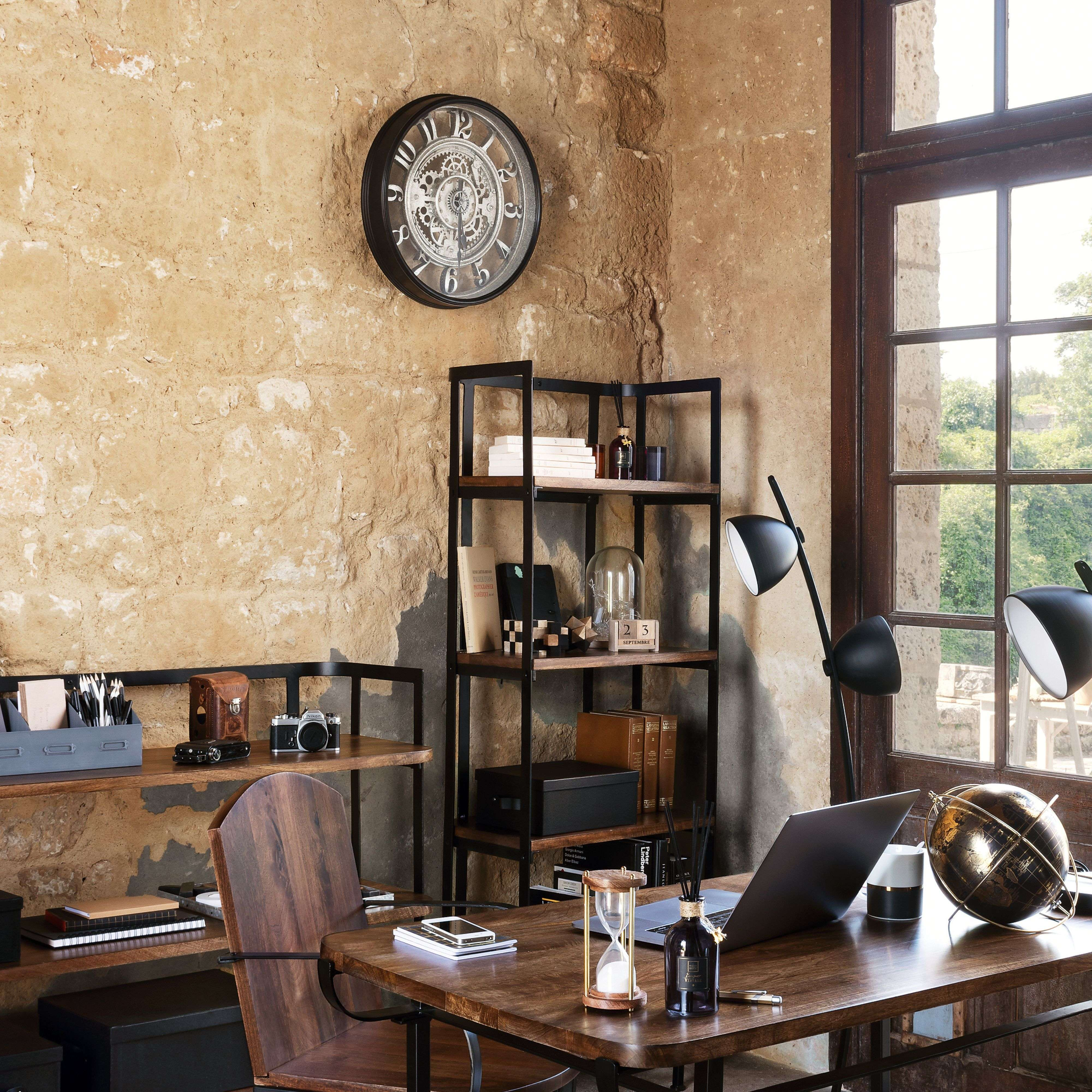 Oficina con escritorio de madera, estantería, reloj, lámpara y ventana.