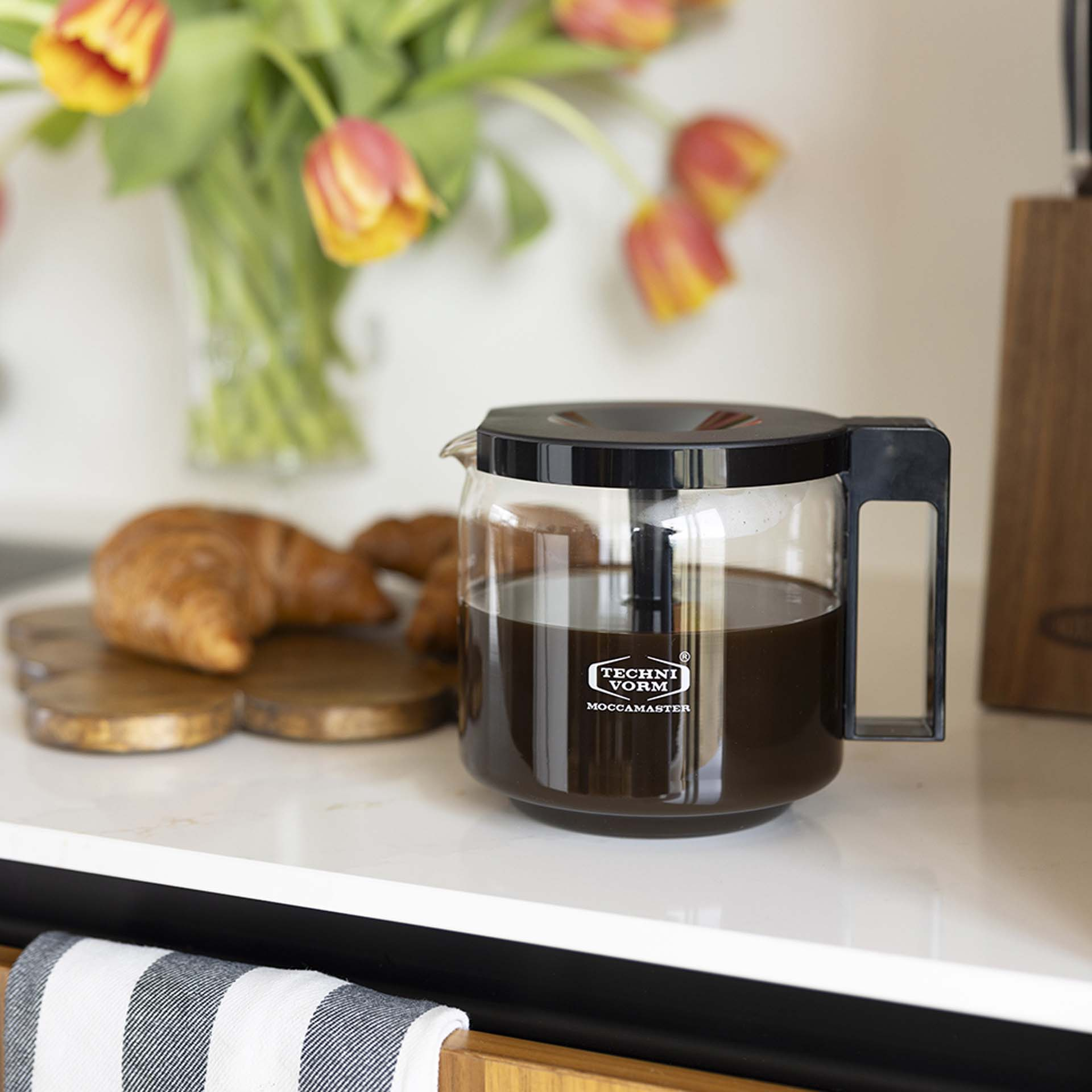 Carafe à café avec café, croissants et tulipes à proximité.