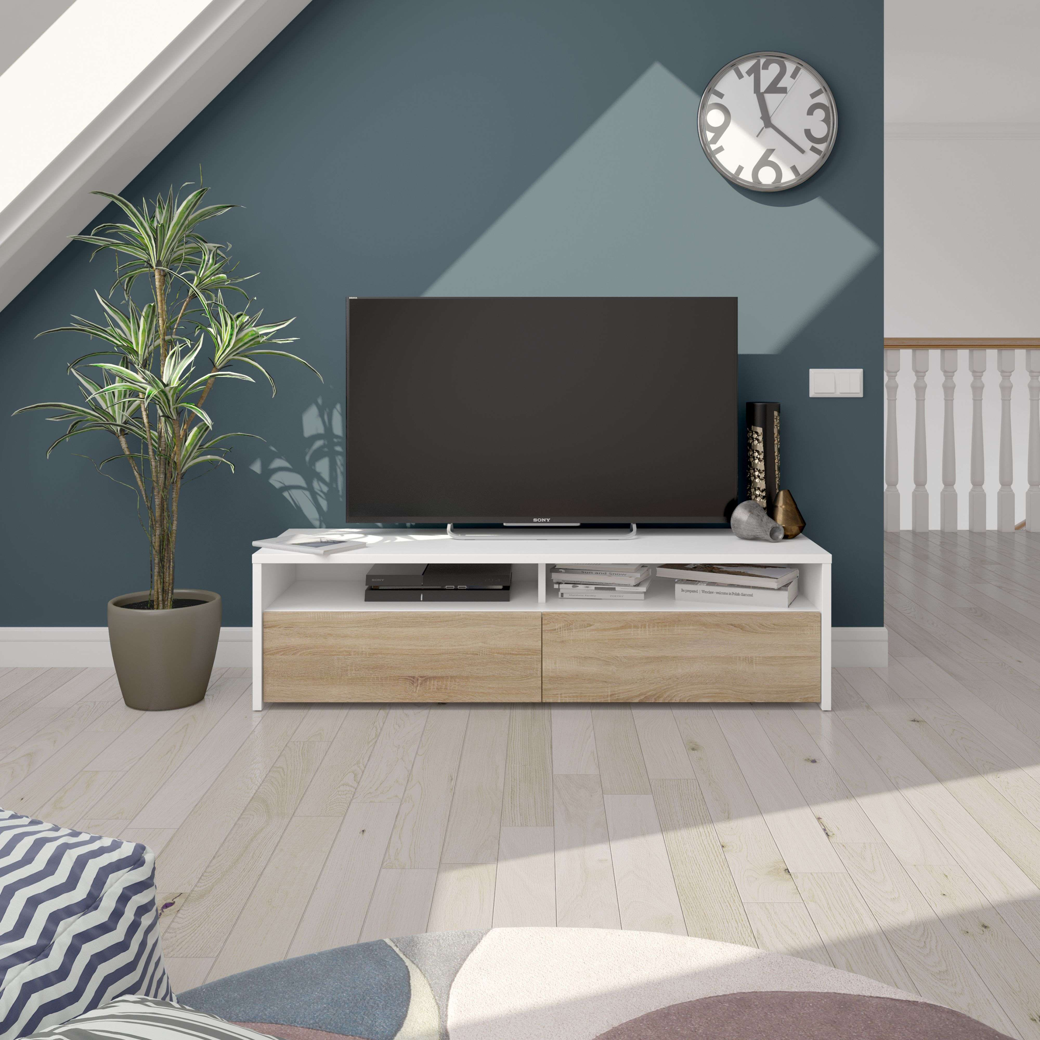 Un televisor está sobre un mueble blanco y de madera. Se ven una planta y un reloj.