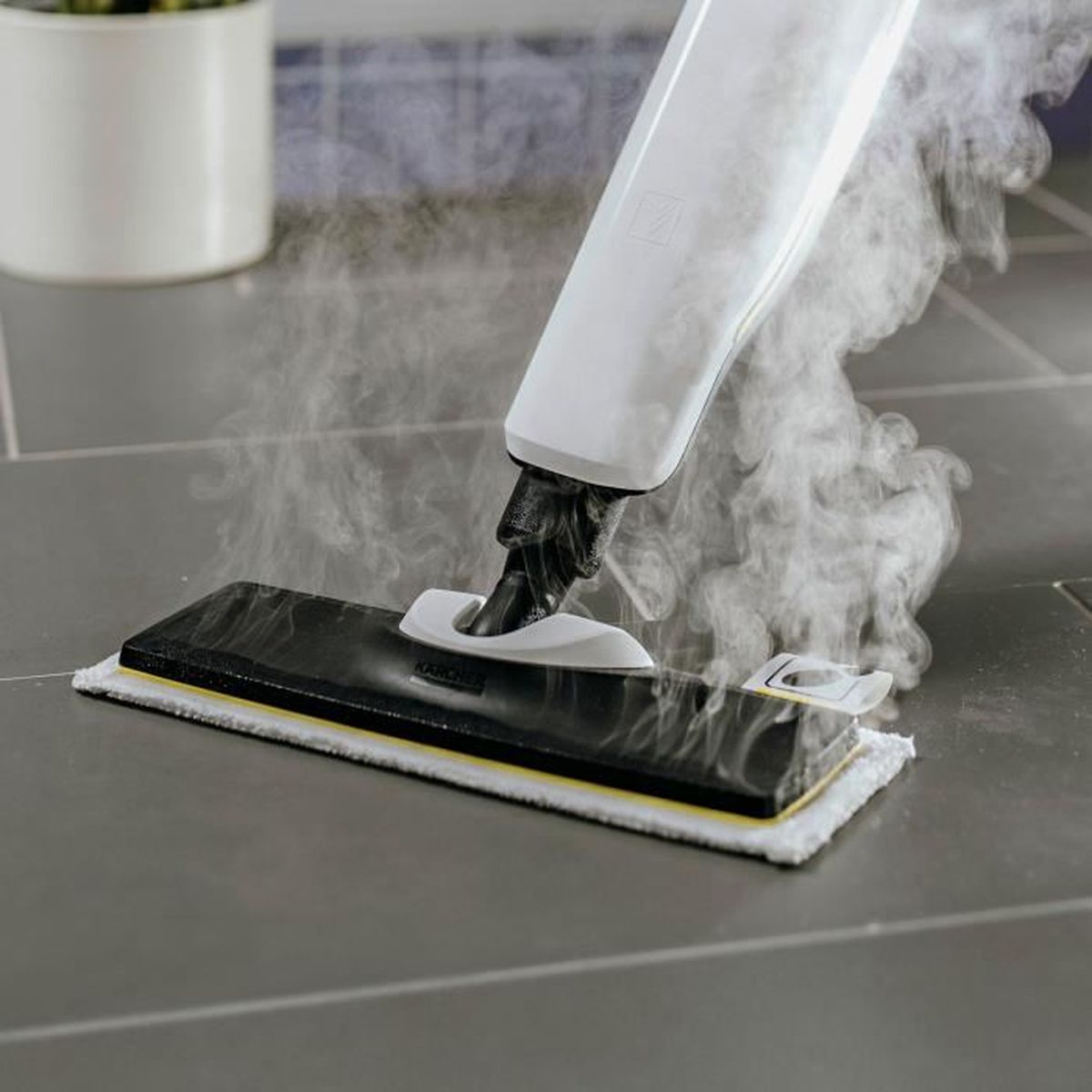 Un pulitore a vapore con manico bianco pulisce un pavimento piastrellato grigio con vapore.