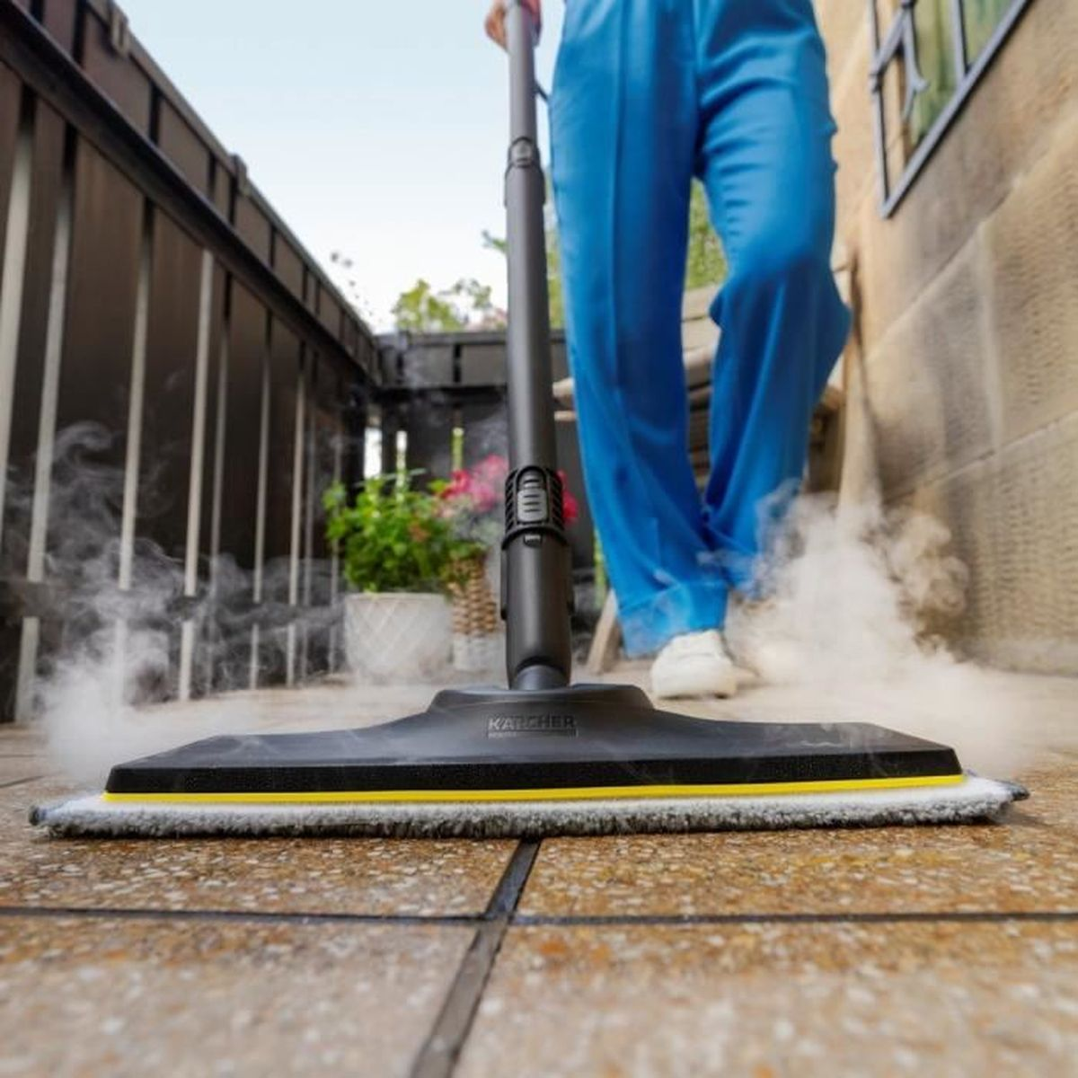 Una persona pulisce un patio con un pulitore a vapore, producendo vapore.