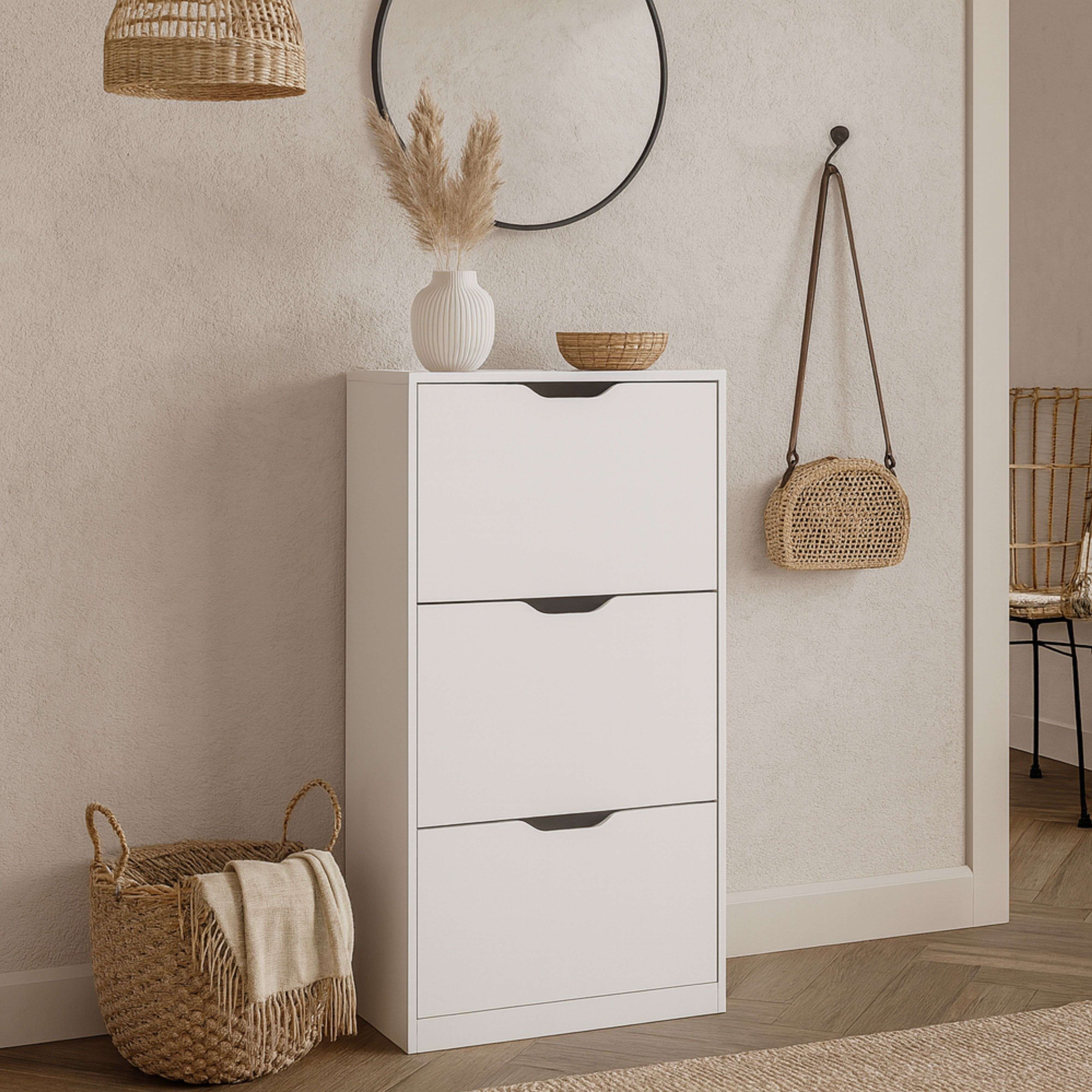Un mueble blanco con tres cajones, una cesta tejida y hierba de la pampa.