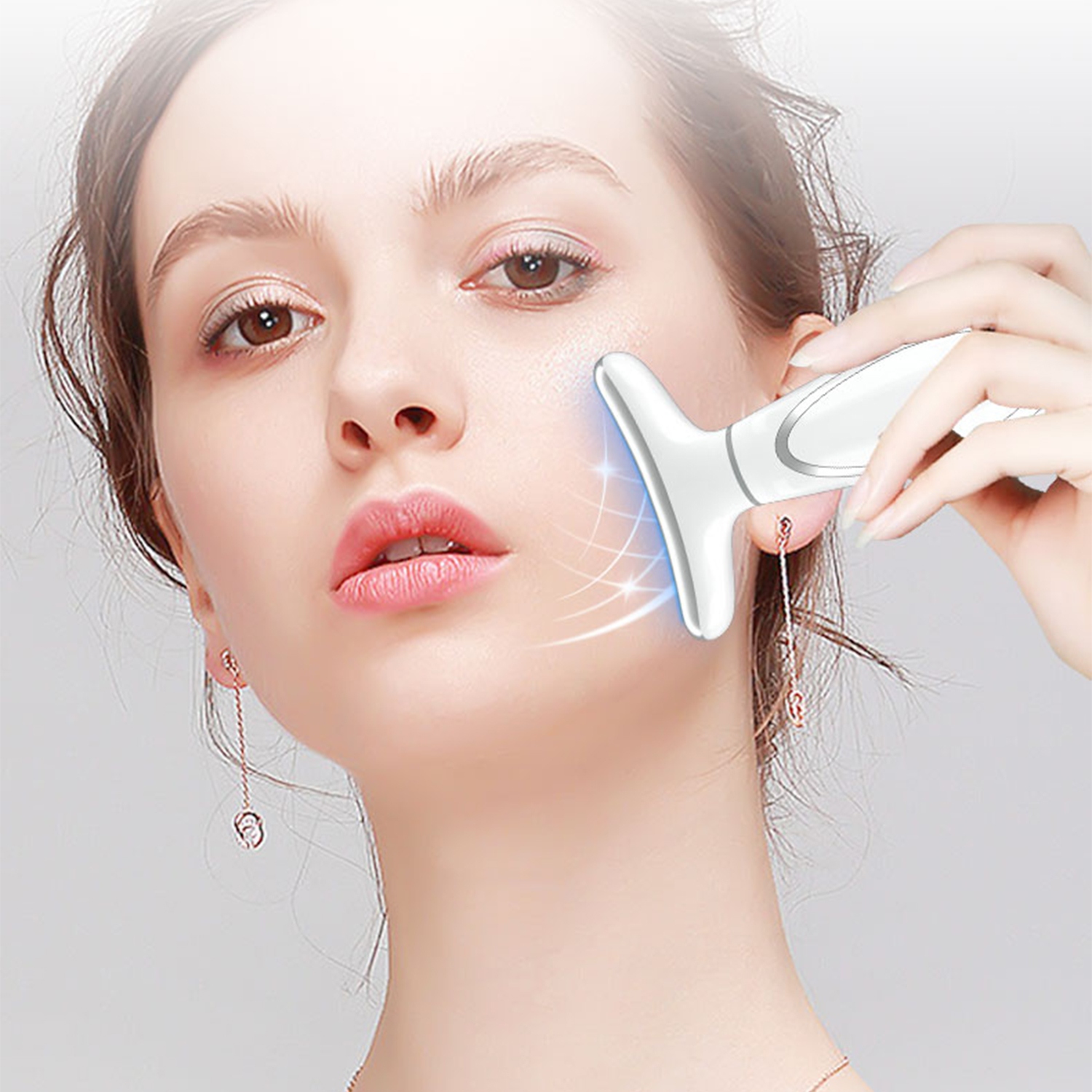Mujer con dispositivo de cuidado de la piel blanco en la mejilla, luces azules, fondo gris.