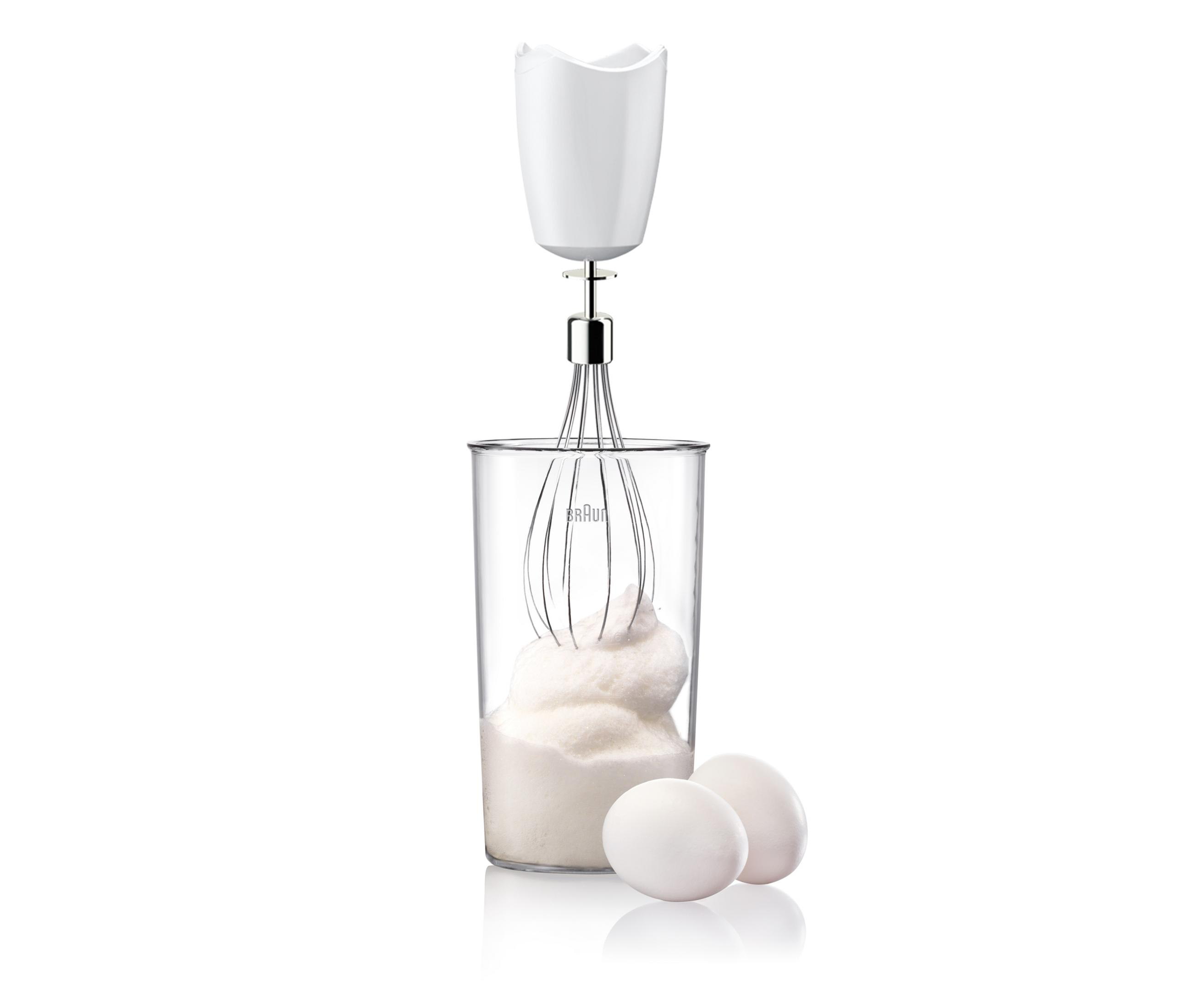 Ein weißer Handmixer schlägt Eiweiß in einem Glas auf. Zwei Eier liegen daneben.