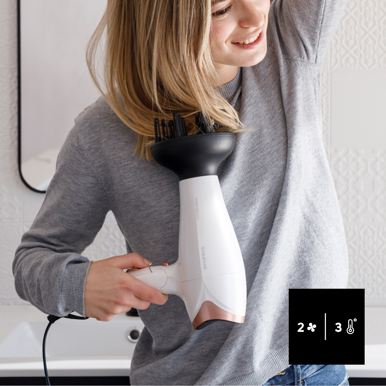 Una mujer se seca el pelo rubio con un secador blanco con difusor.