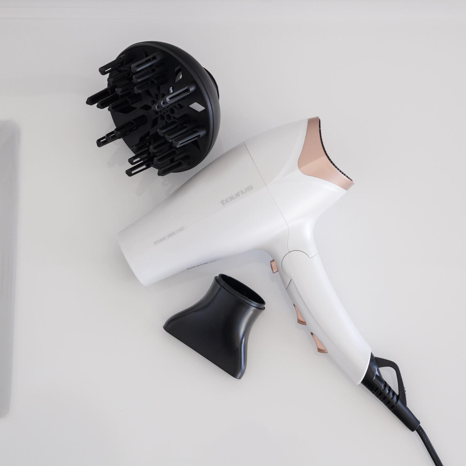 Secador de pelo blanco con detalles en oro rosa, difusor negro y boquilla concentradora negra.