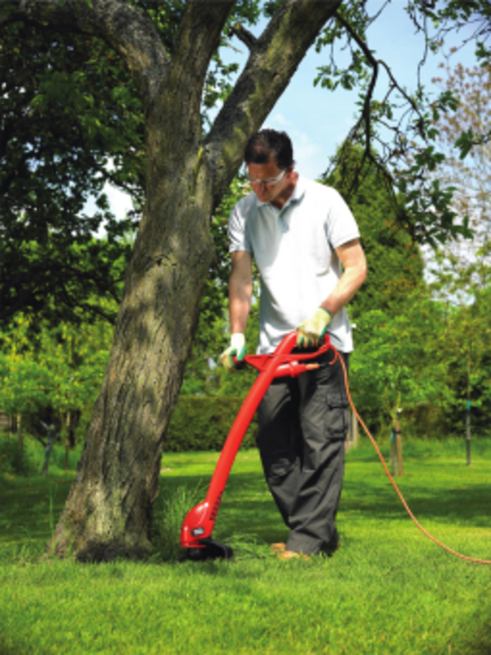 Mann trimmt Gras am Baum mit rotem Trimmer.