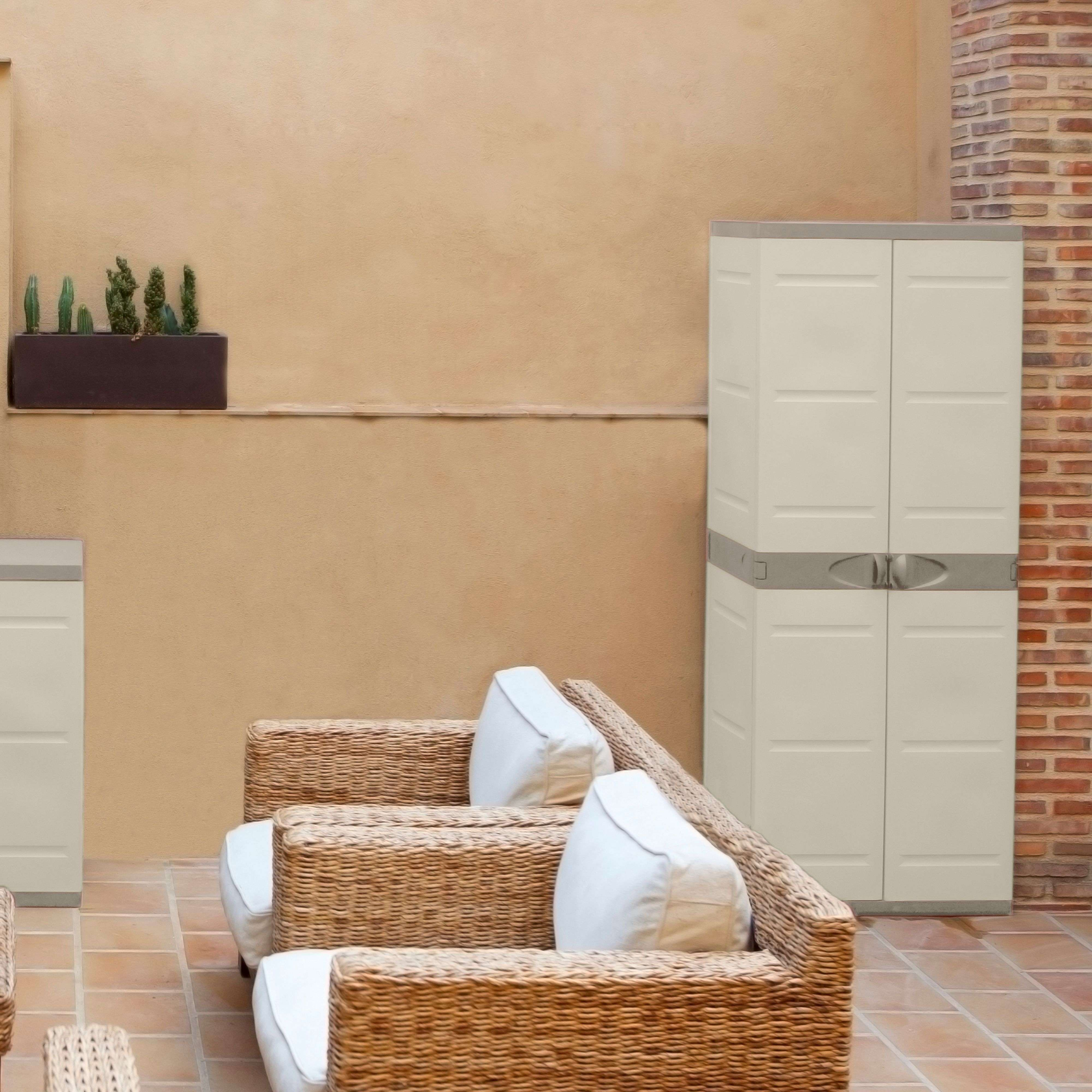 Un armario beige junto a un pilar de ladrillo, con muebles de mimbre y cactus delante.