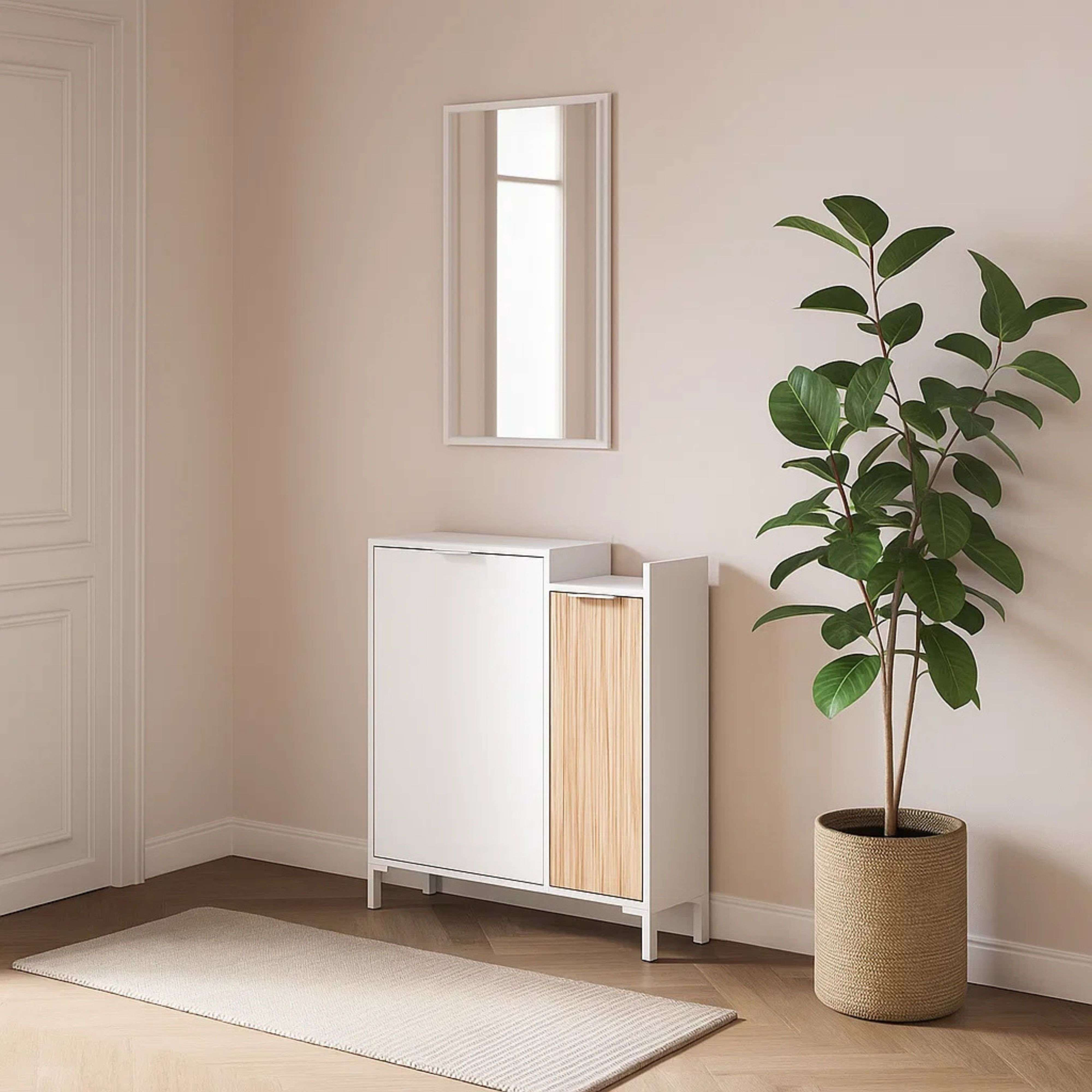 Un zapatero blanco con acento de madera, espejo encima, planta en cesta al lado.