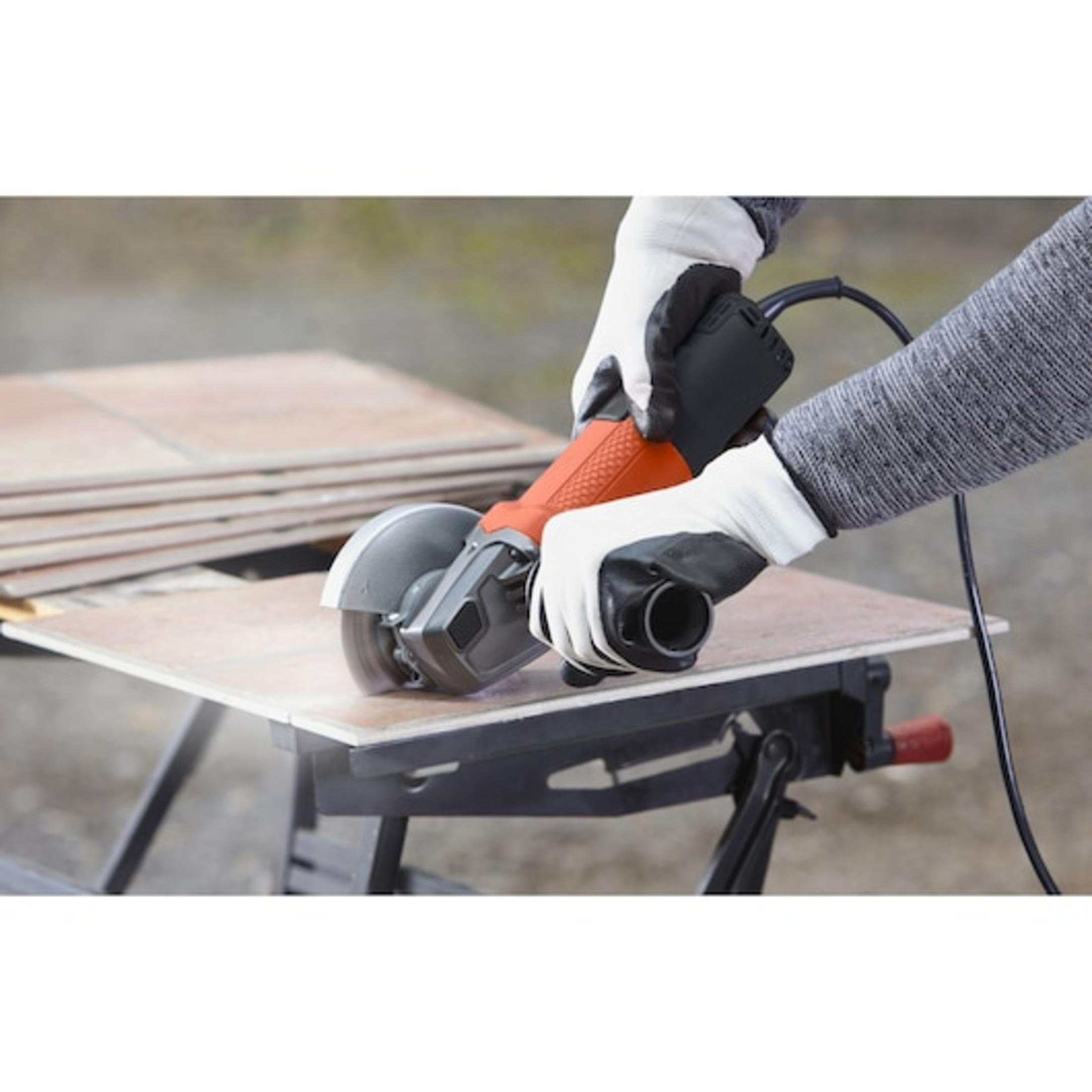 Person mit Handschuhen schneidet Fliese mit Winkelschleifer auf einem Tisch.