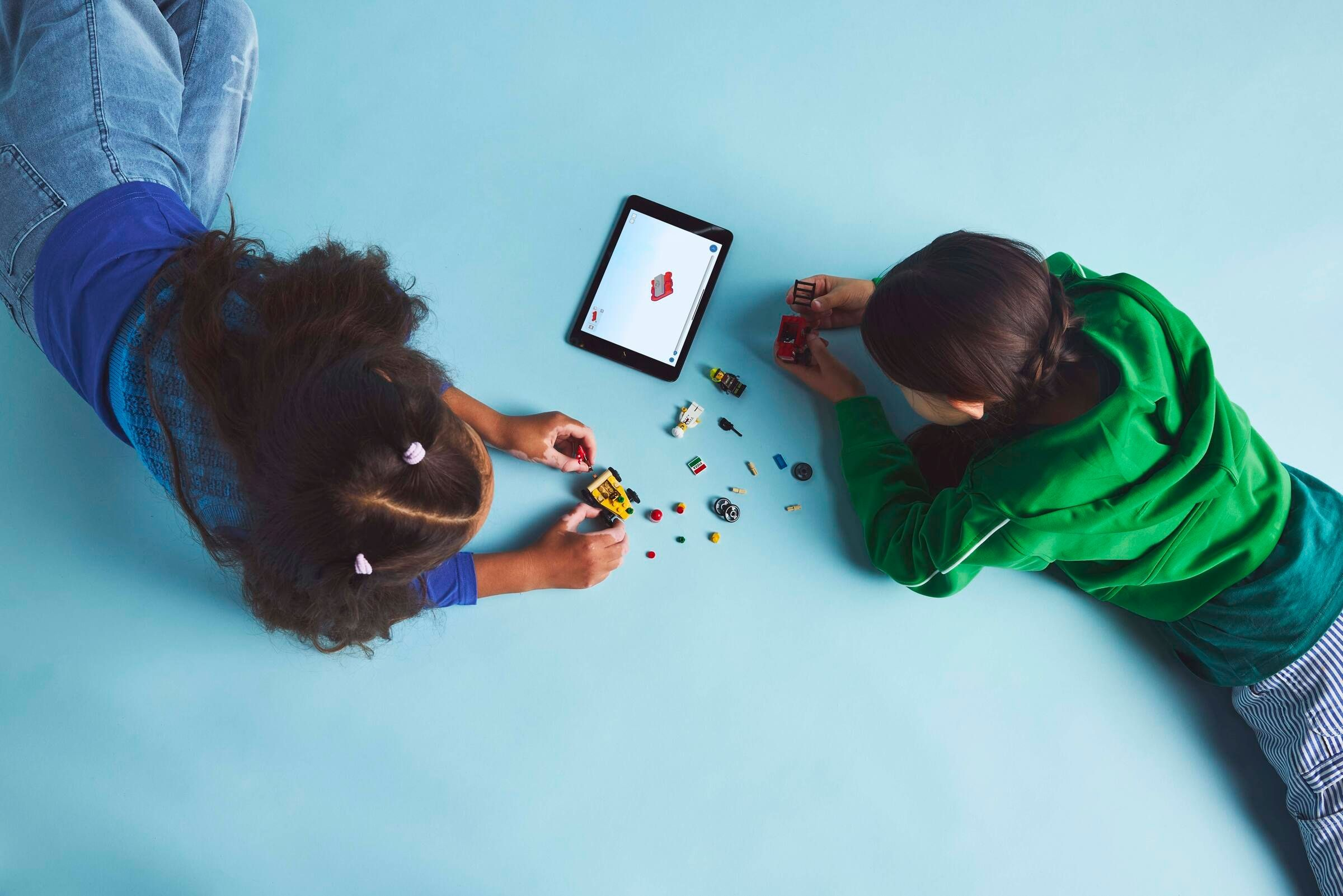 Zwei Kinder bauen mit Legosteinen nach Anleitung auf einem Tablet.
