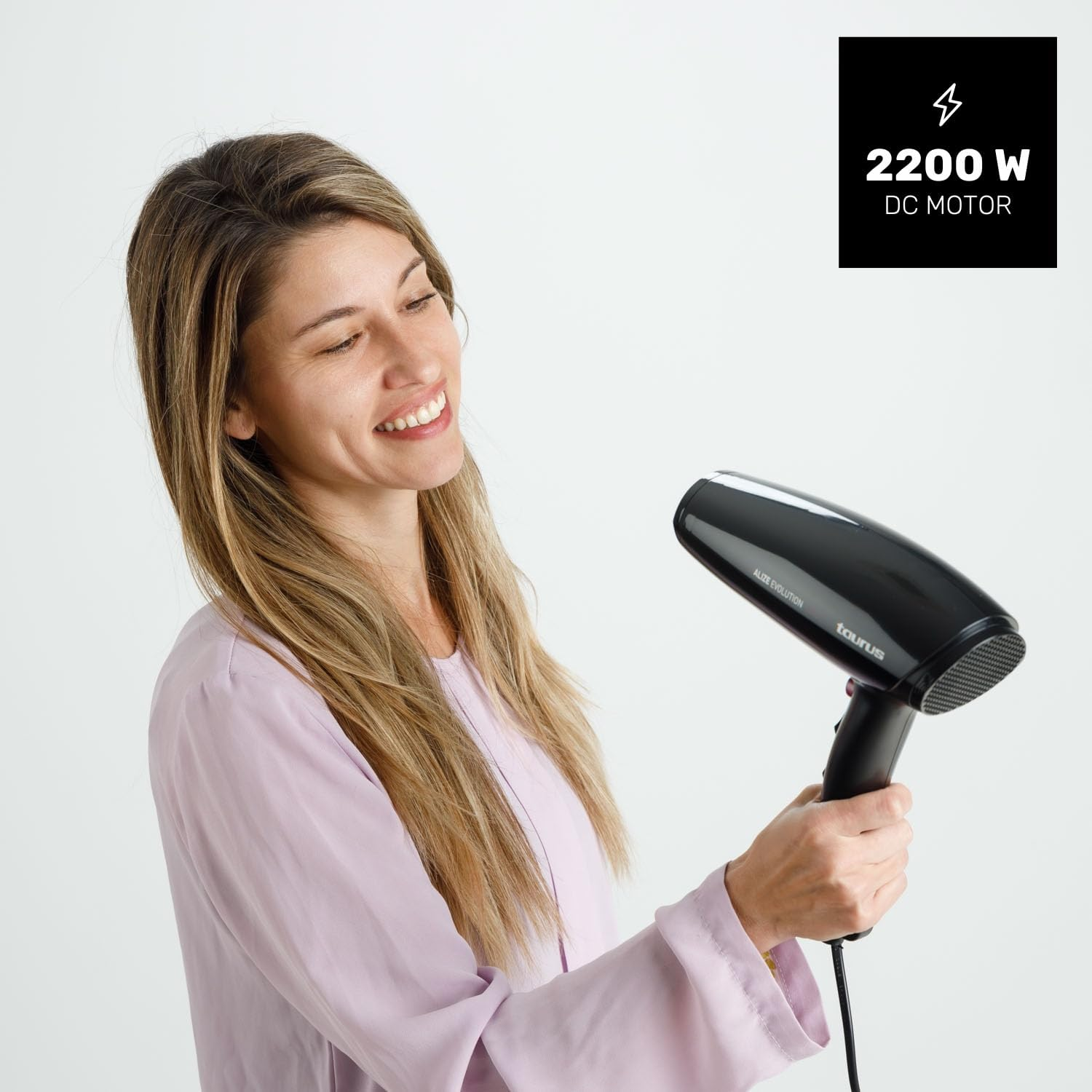 Una mujer de pelo largo y rubio sostiene un secador de pelo negro.