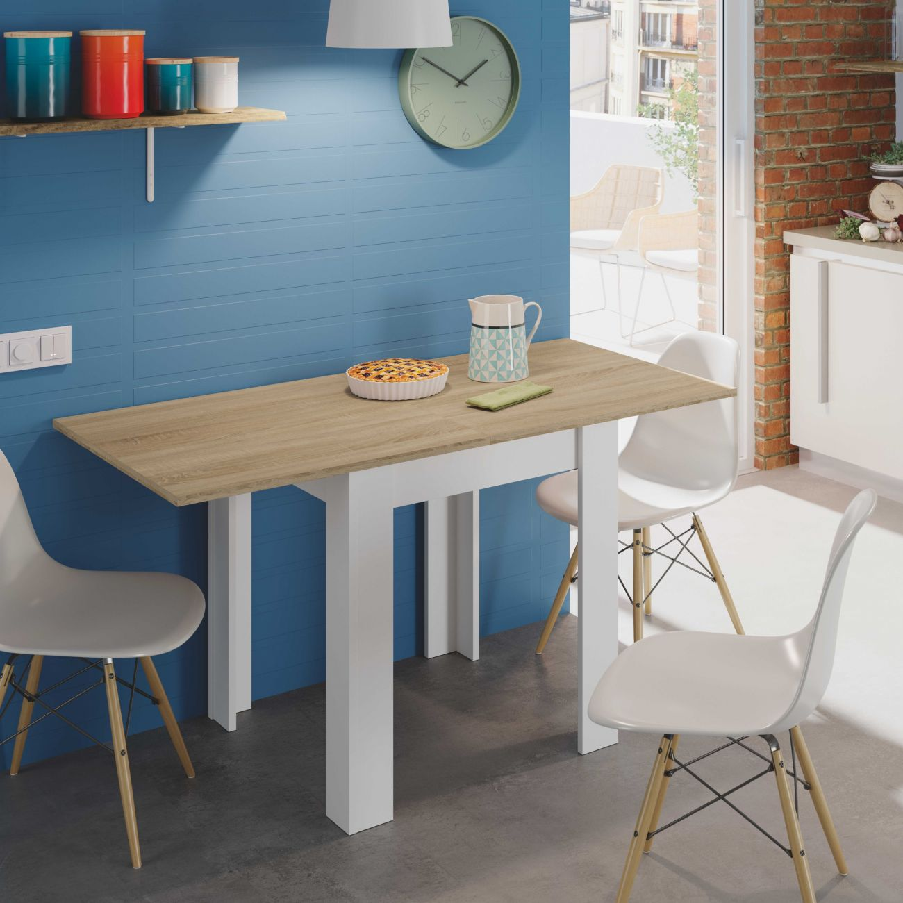 Una mesa de comedor con pastel y jarra, rodeada de sillas blancas, con pared azul.