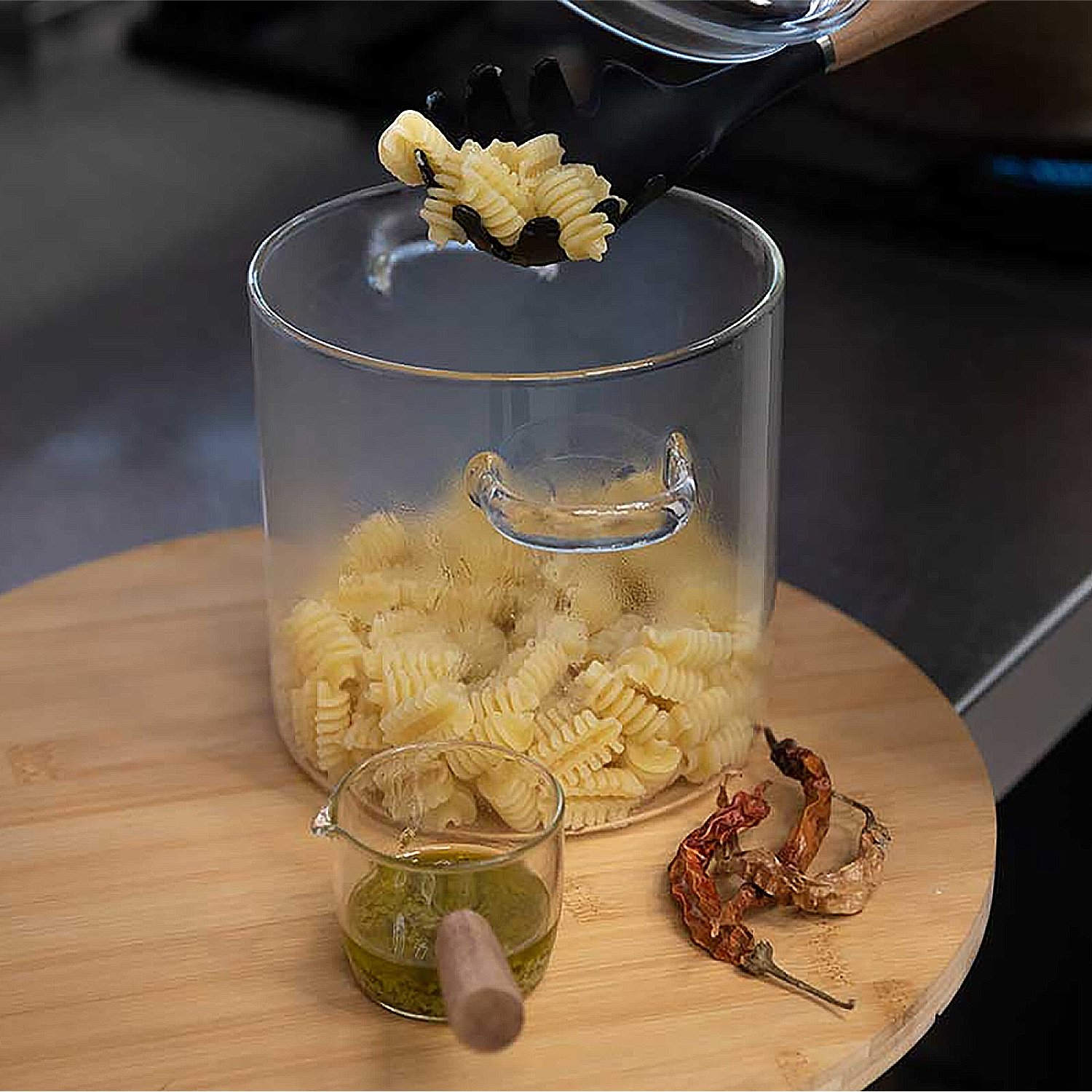 Pinzas colocan pasta en espiral en un frasco de vidrio. Un vaso pequeño contiene salsa verde.