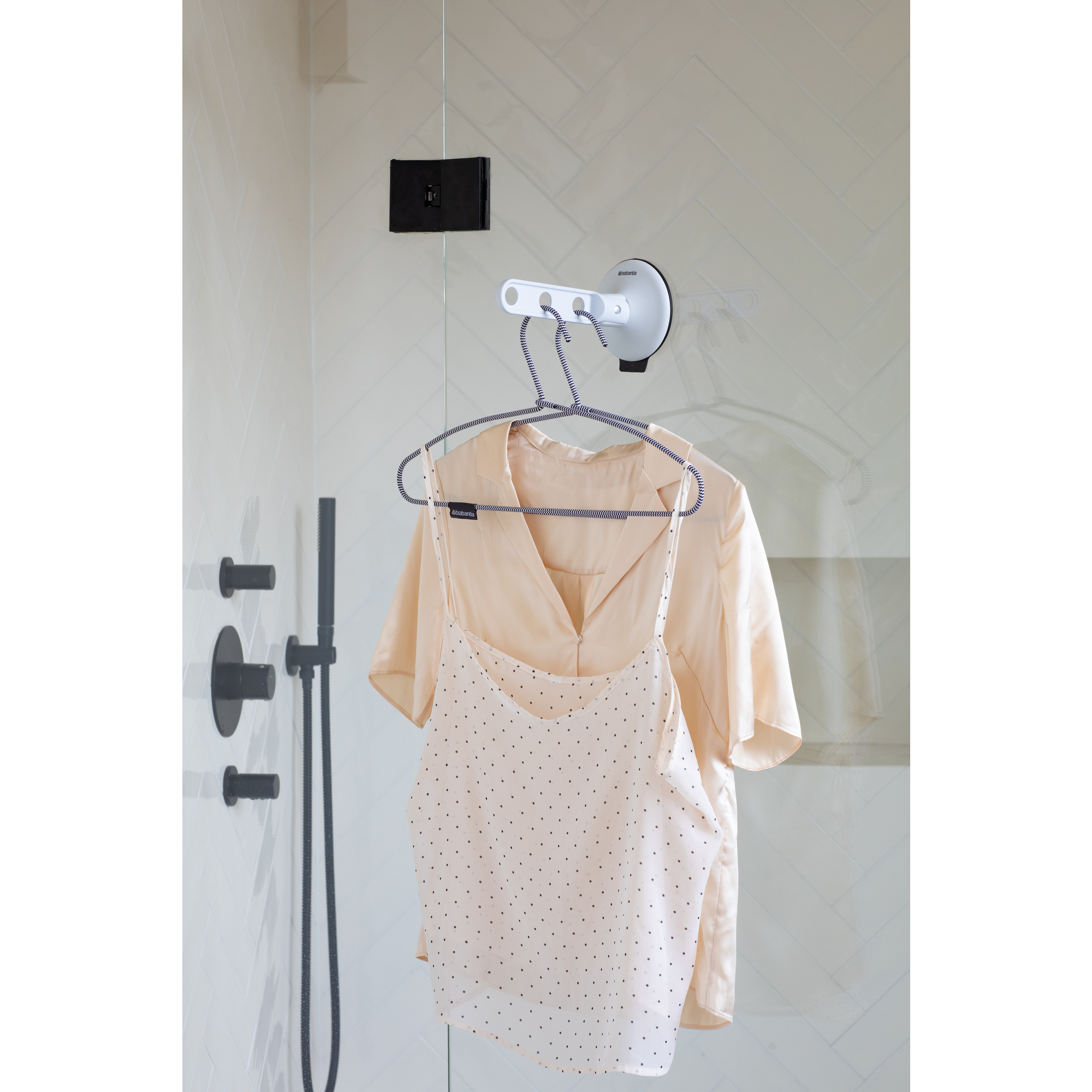 Two garments hang on a hanger in a shower.