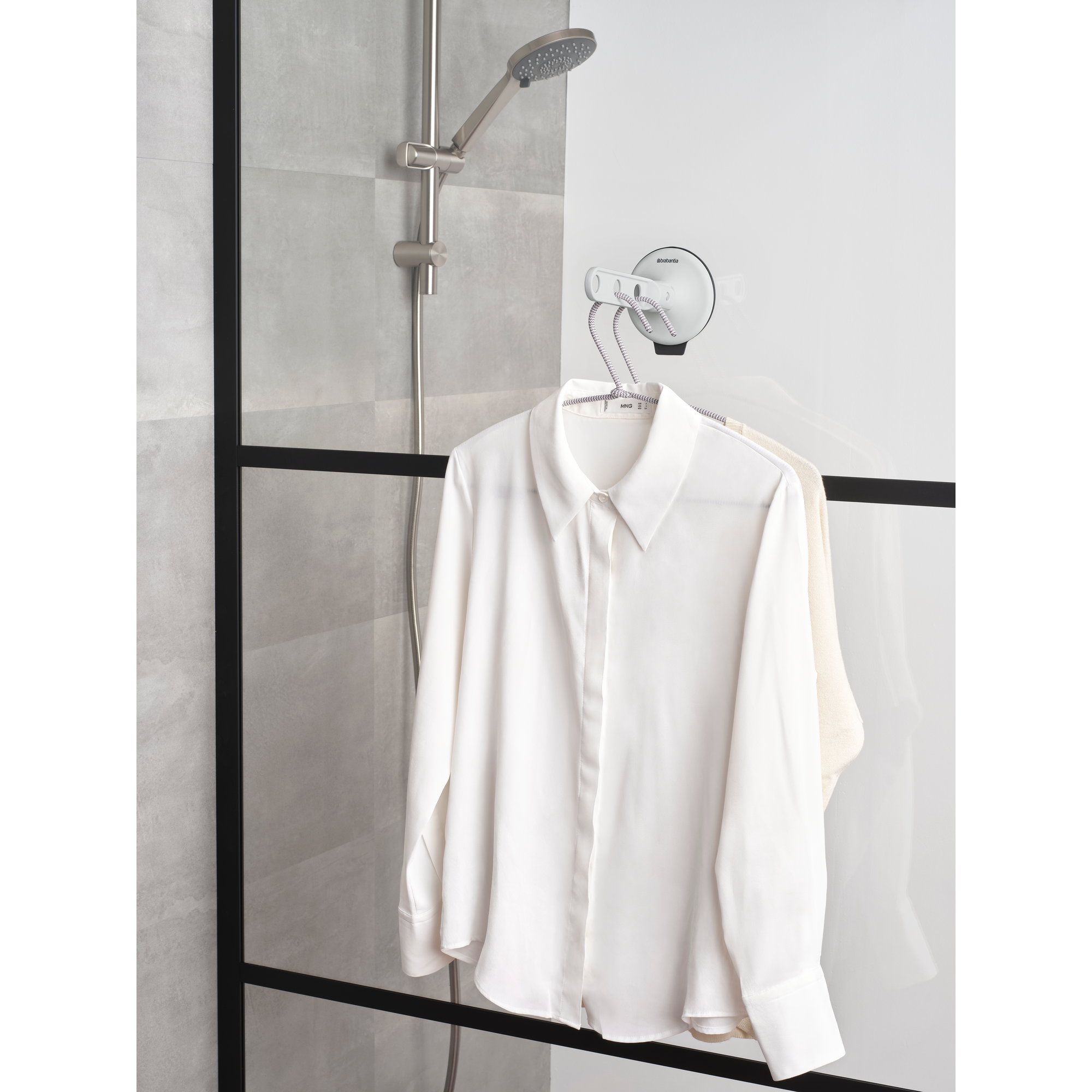 A white shirt and a cream sweater hang on a hanger in the shower.