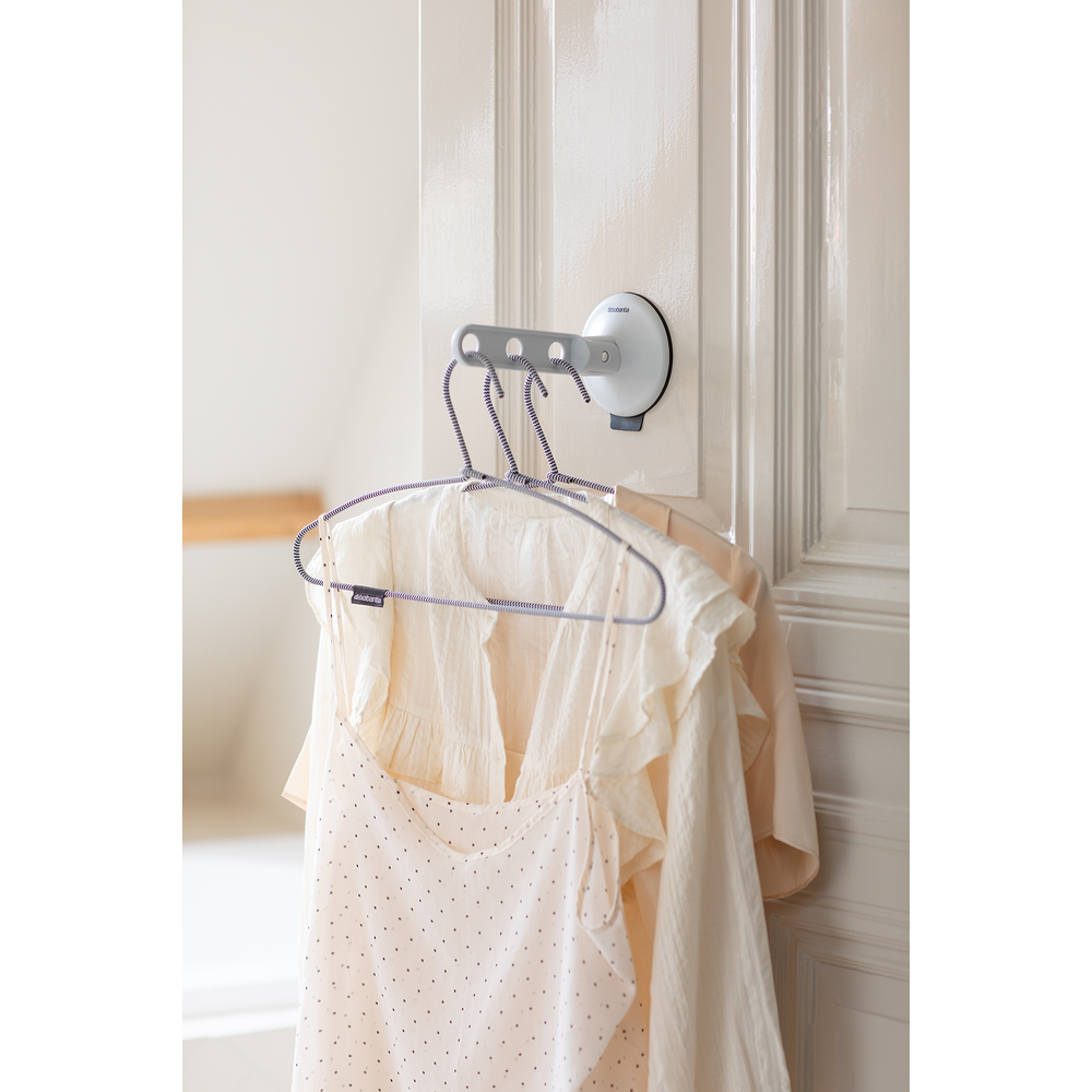 A hanger with two garments hangs on a door hook attached to a white door.