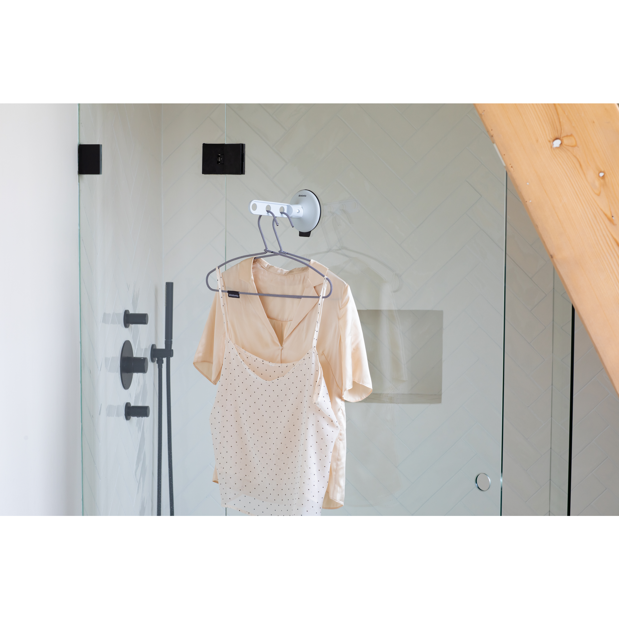 A white Brabantia drying rack holds two light-colored garments in a modern shower.