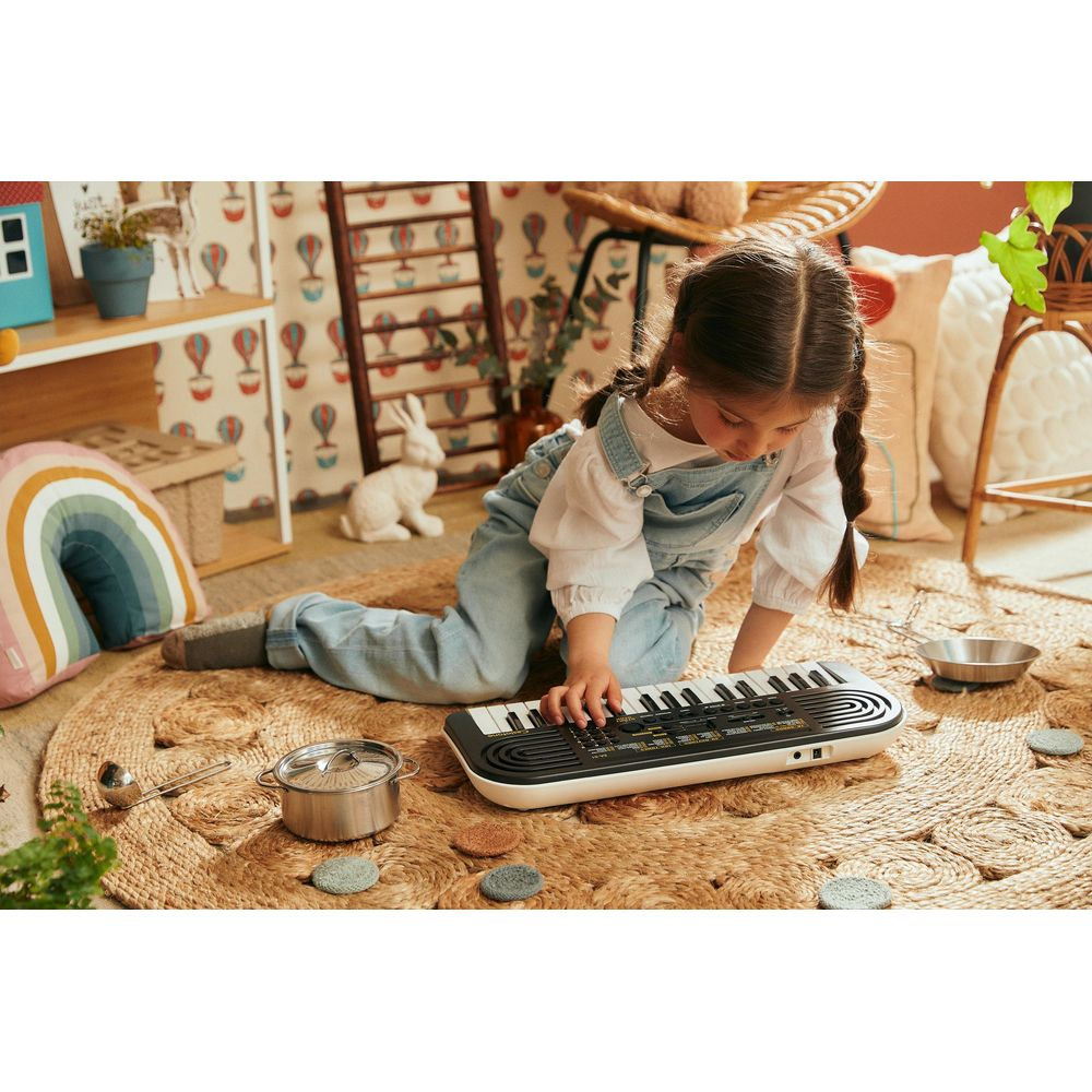 A young girl plays a keyboard on a rug, surrounded by toys and decor.