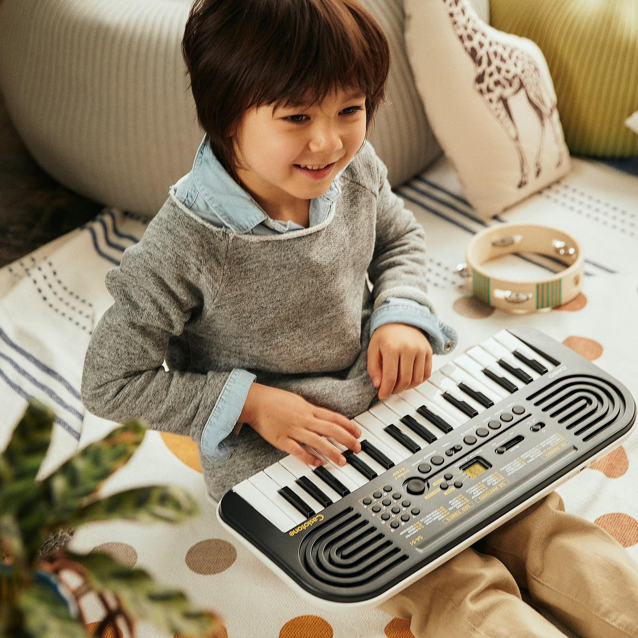 A boy plays a portable keyboard while sitting on a blanket.