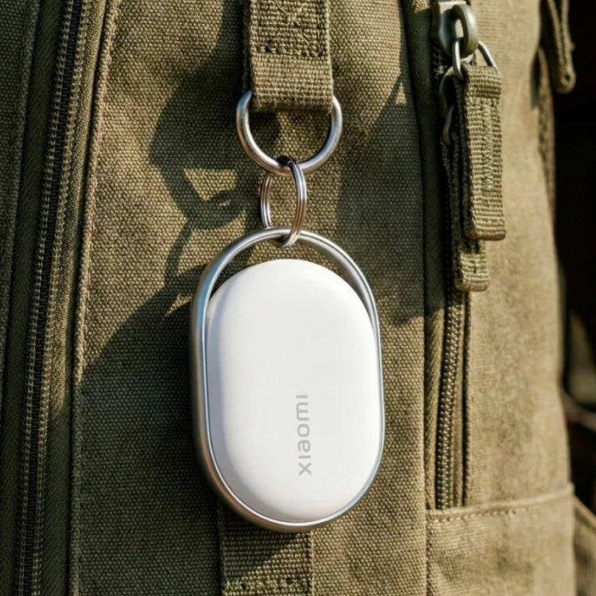 Beyaz bir Xiaomi anahtarlık yeşil bir çantaya asılı.