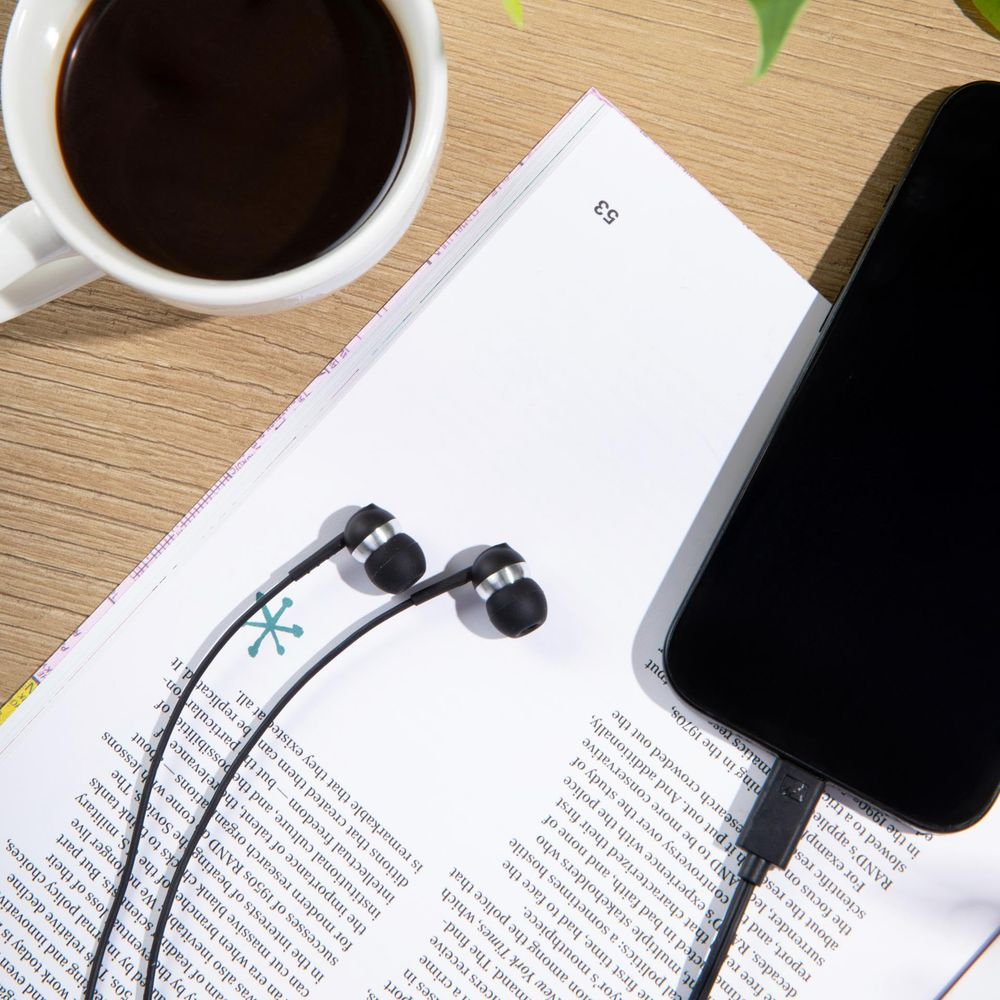Una tazza di caffè, cuffie e uno smartphone giacciono su una rivista aperta.