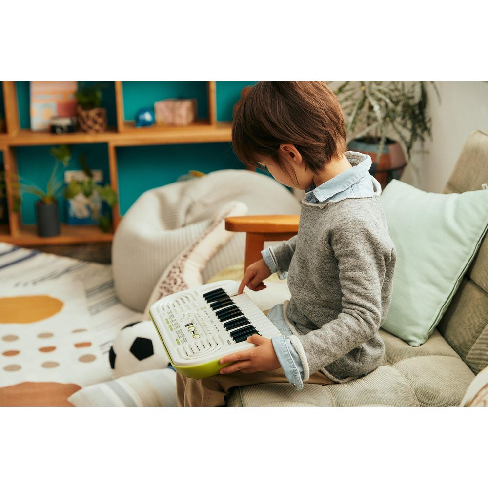 Een kind bespeelt een klein keyboard in een woonkamer.