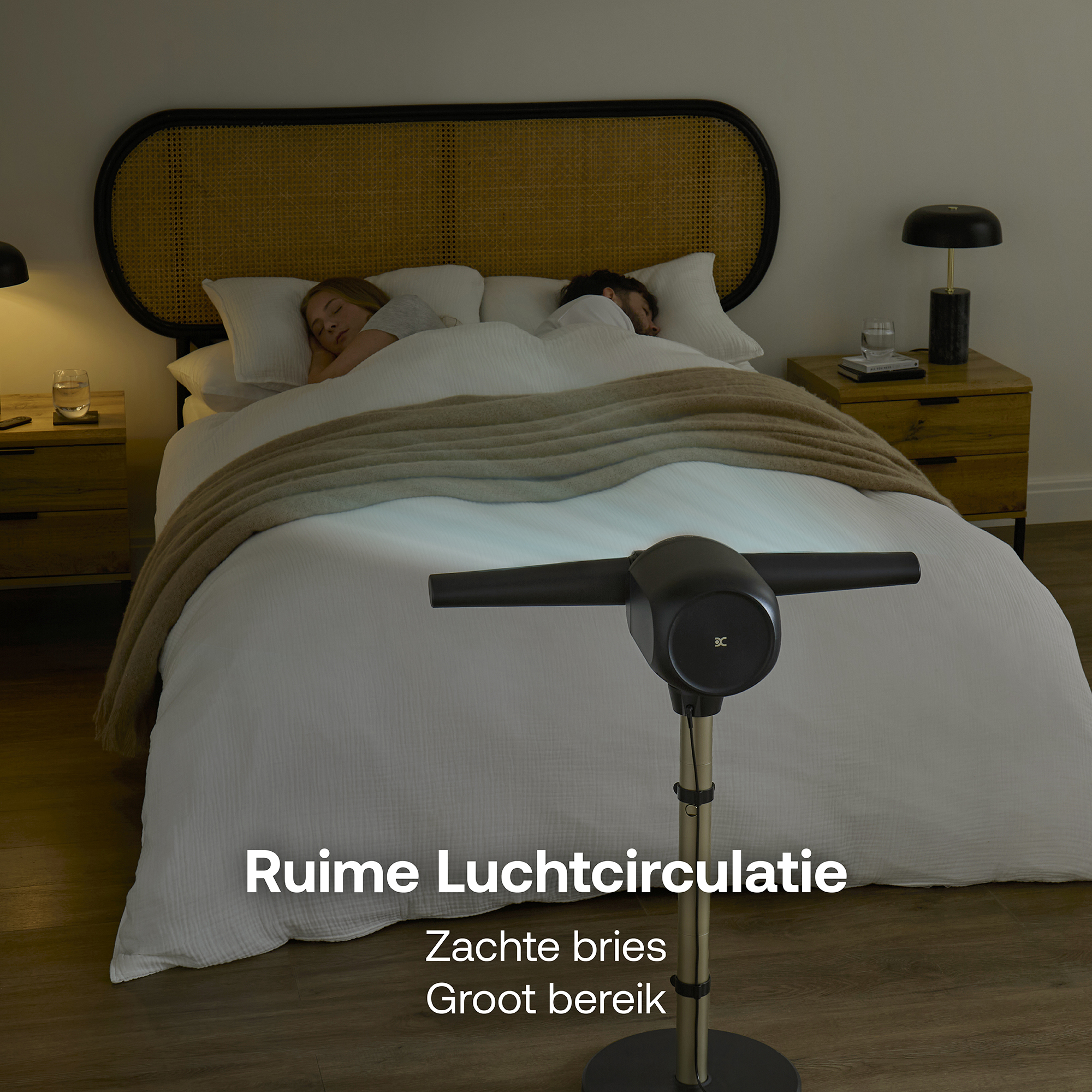 Een man en vrouw slapen in bed. Een ventilator staat op de voorgrond.