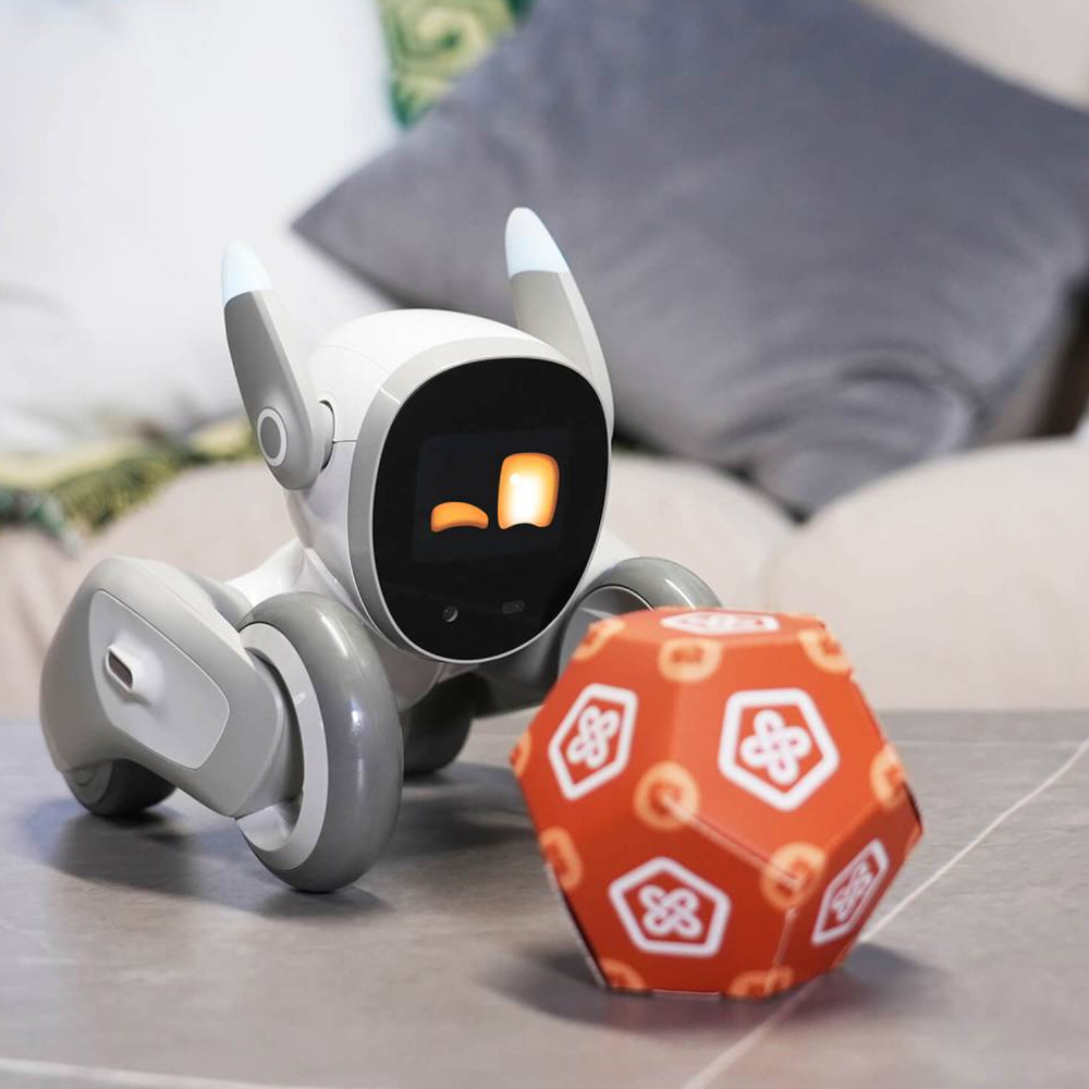 Ein weißer Roboter mit Rädern und einem Bildschirm spielt mit einem roten Ball mit weißen Symbolen.