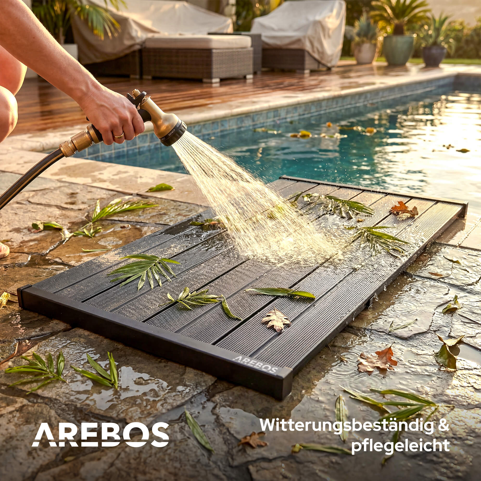 Eine Hand sprüht Wasser auf eine dunkle Matte neben einem Pool.