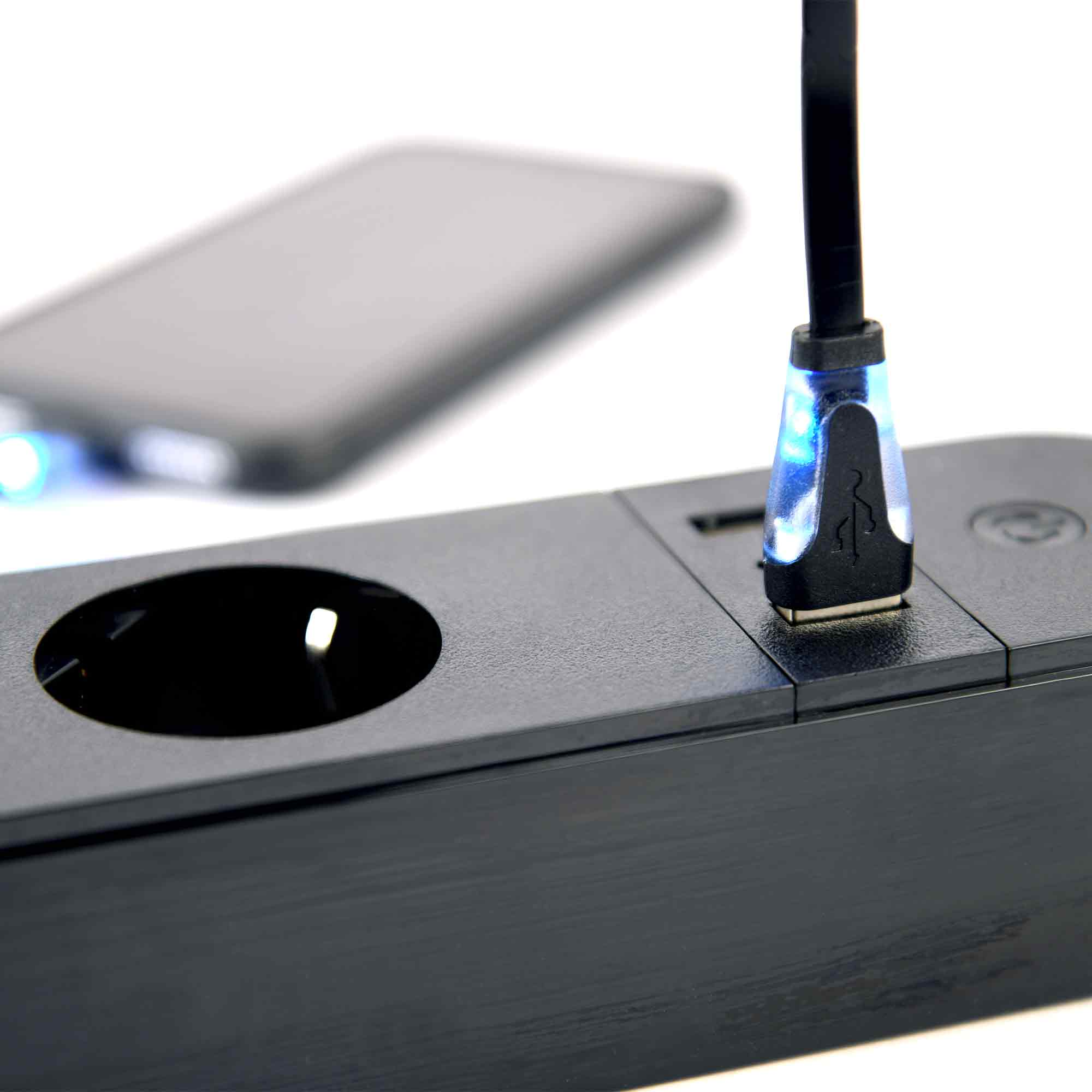 Schwarze Ladestation mit eingestecktem USB-Kabel und einem Smartphone daneben.