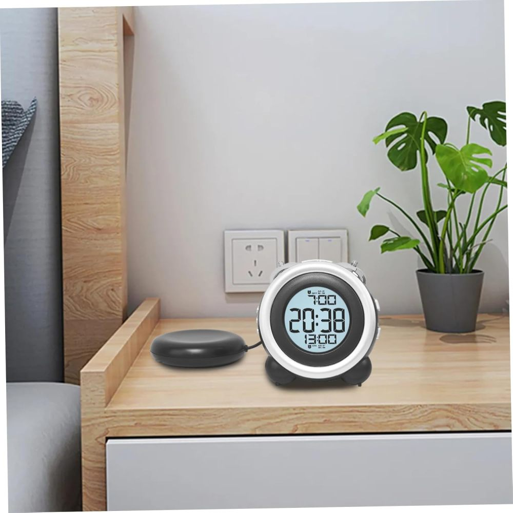 Digitaler Wecker mit schwarzem Vibrationspad auf einem Nachttisch neben einer Pflanze.