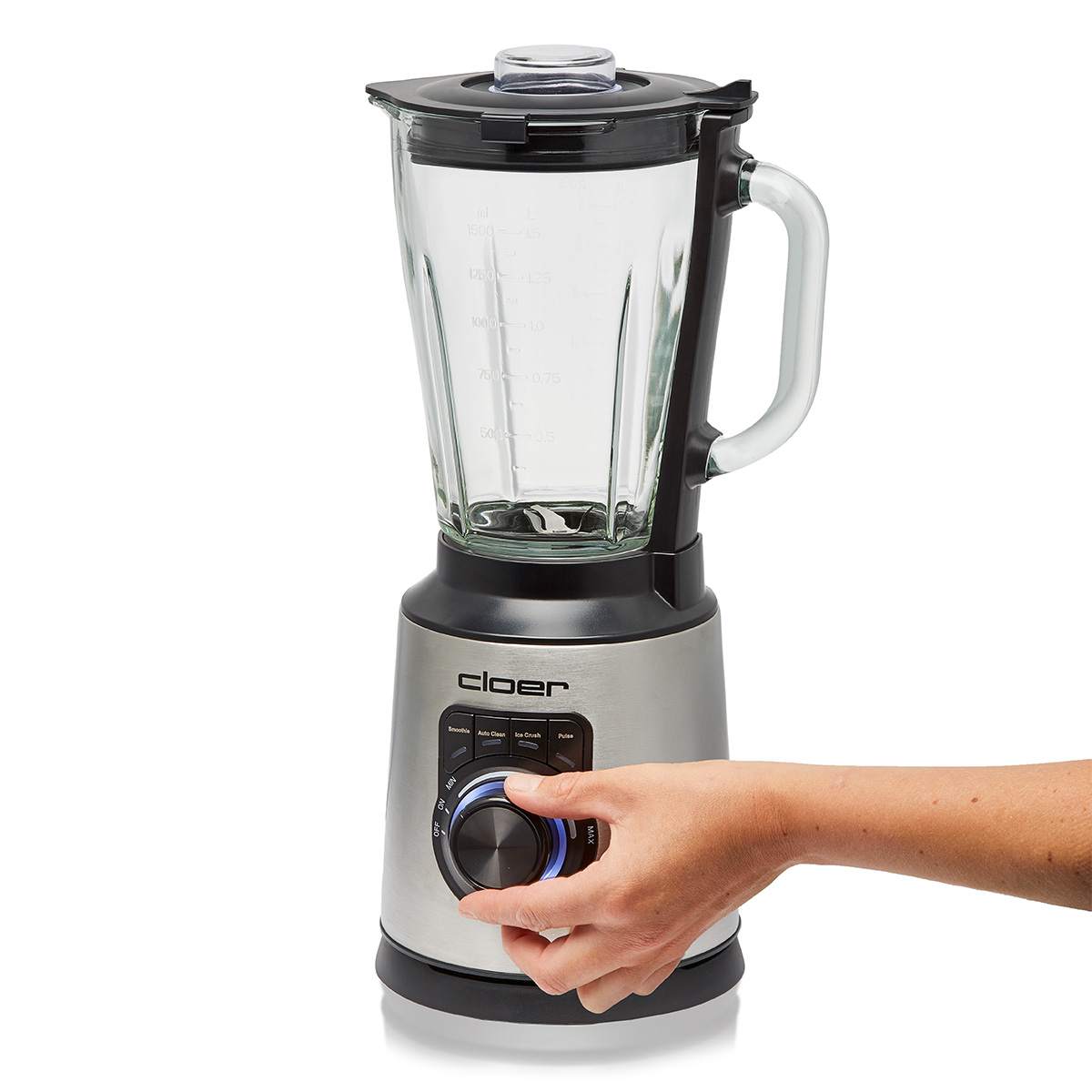 Eine Hand dreht einen Knopf an einem silbernen und schwarzen Mixer mit Glasbehälter.