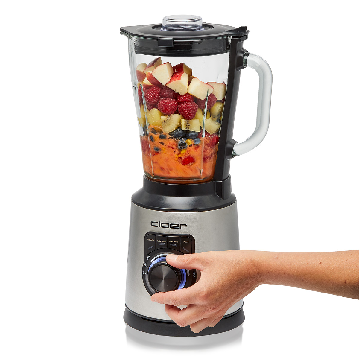 Ein Mixer mit Obst und einer Hand, die den Knopf bedient.