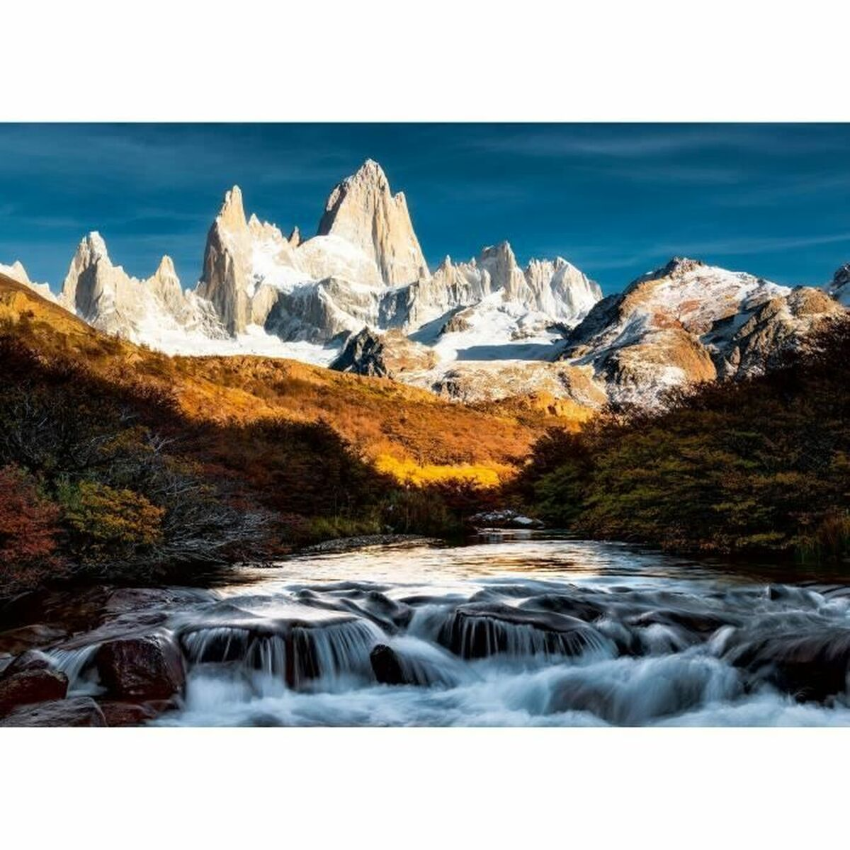 Un torrente di montagna che scorre passa tra formazioni rocciose, con vette innevate sullo sfondo.
