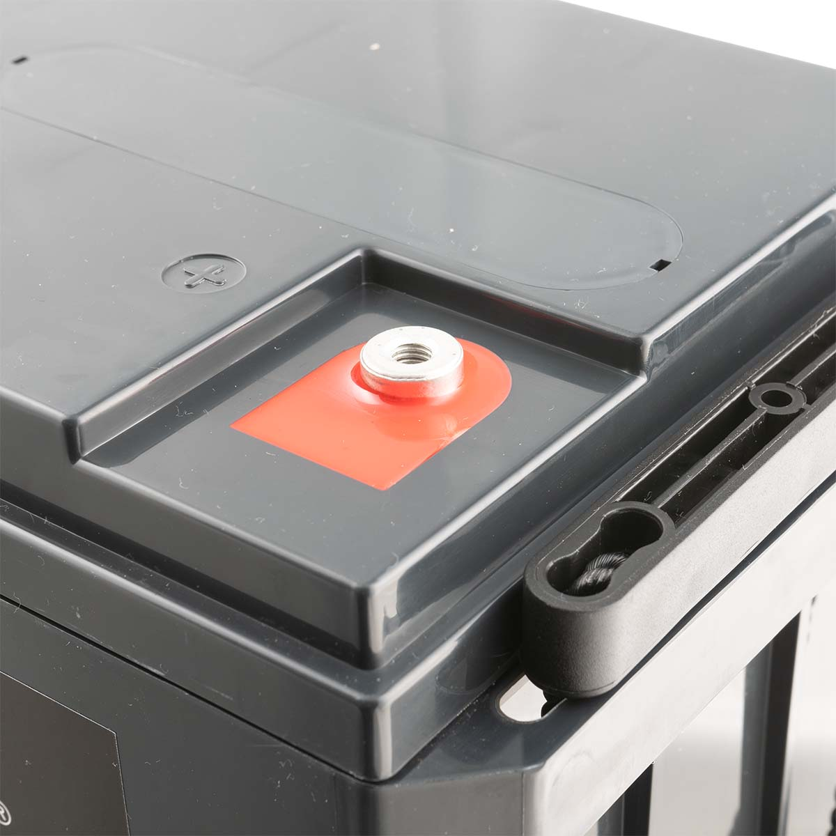 Nahaufnahme eines grauen Autobatterieanschlusses mit roter Akzentuierung und Metallbolzen.