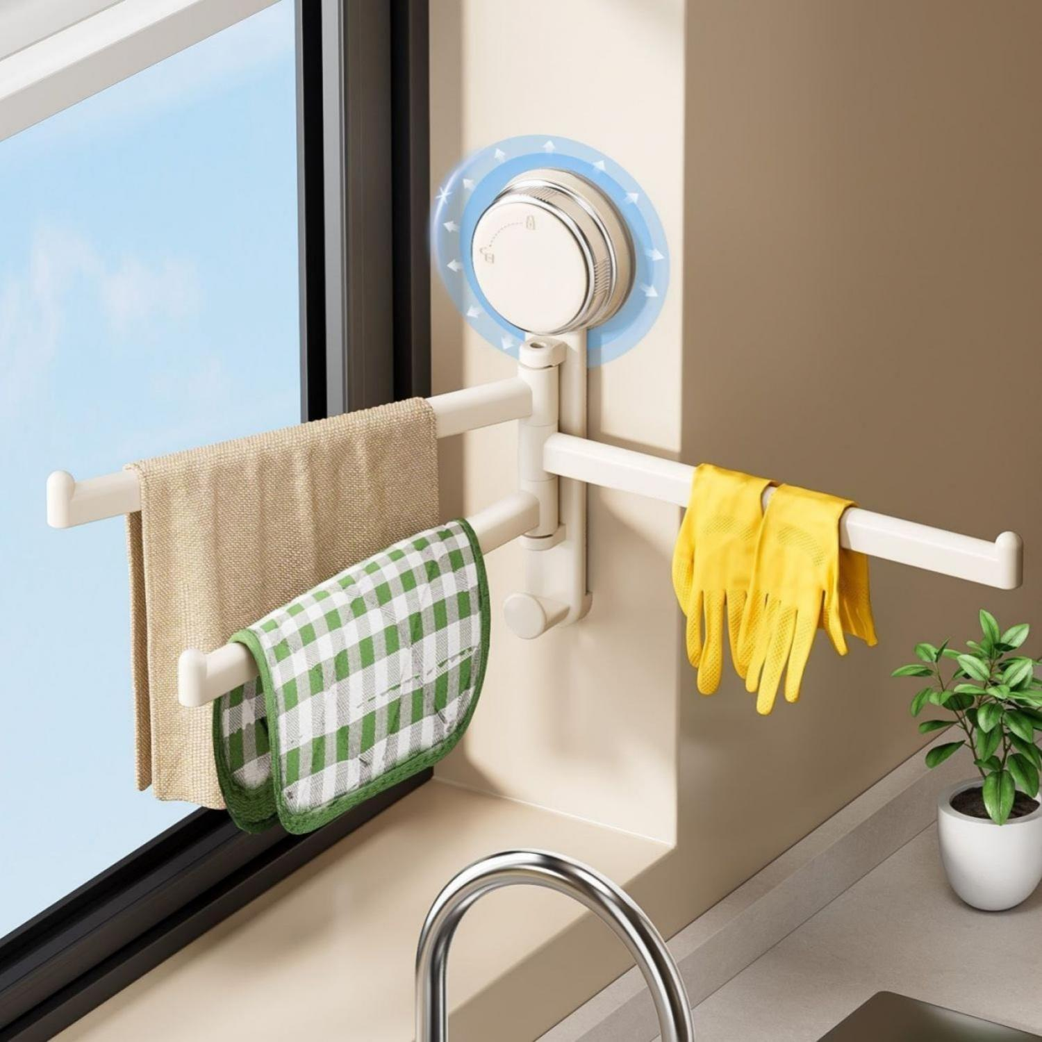 Ein weißer Saugnapfständer hält zwei Handtücher, gelbe Handschuhe und ein grün kariertes Tuch am Fenster.