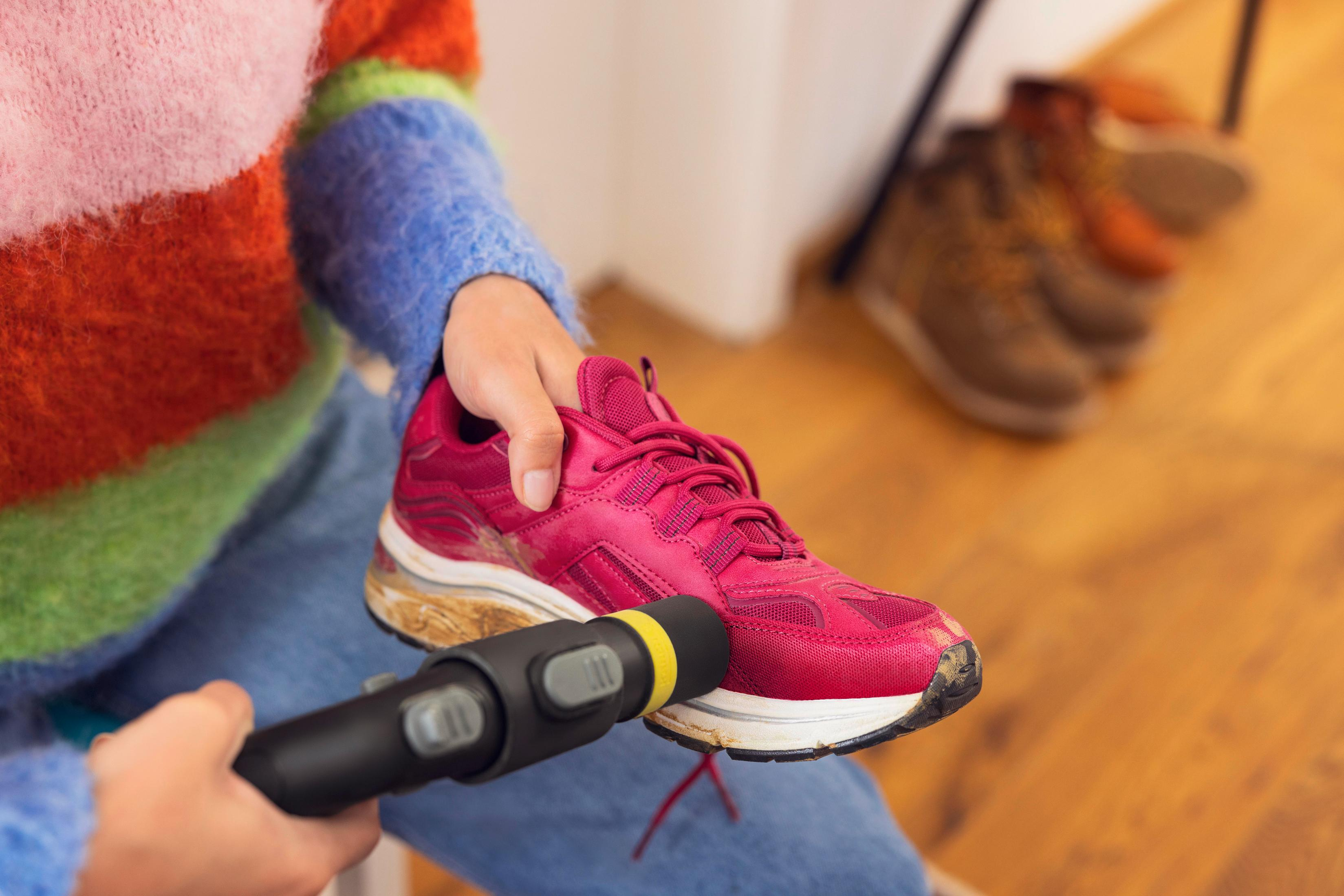 Una persona pulisce una scarpa da ginnastica rosa sporca con un dispositivo nero.