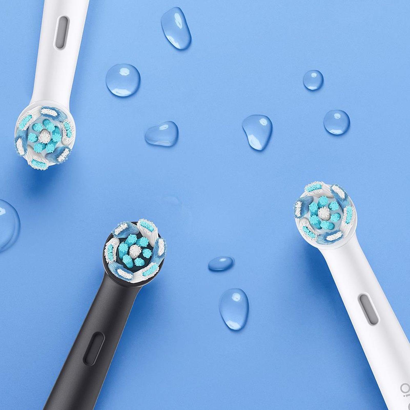 Tre testine di spazzolino con setole blu e bianche su sfondo blu con gocce d'acqua.