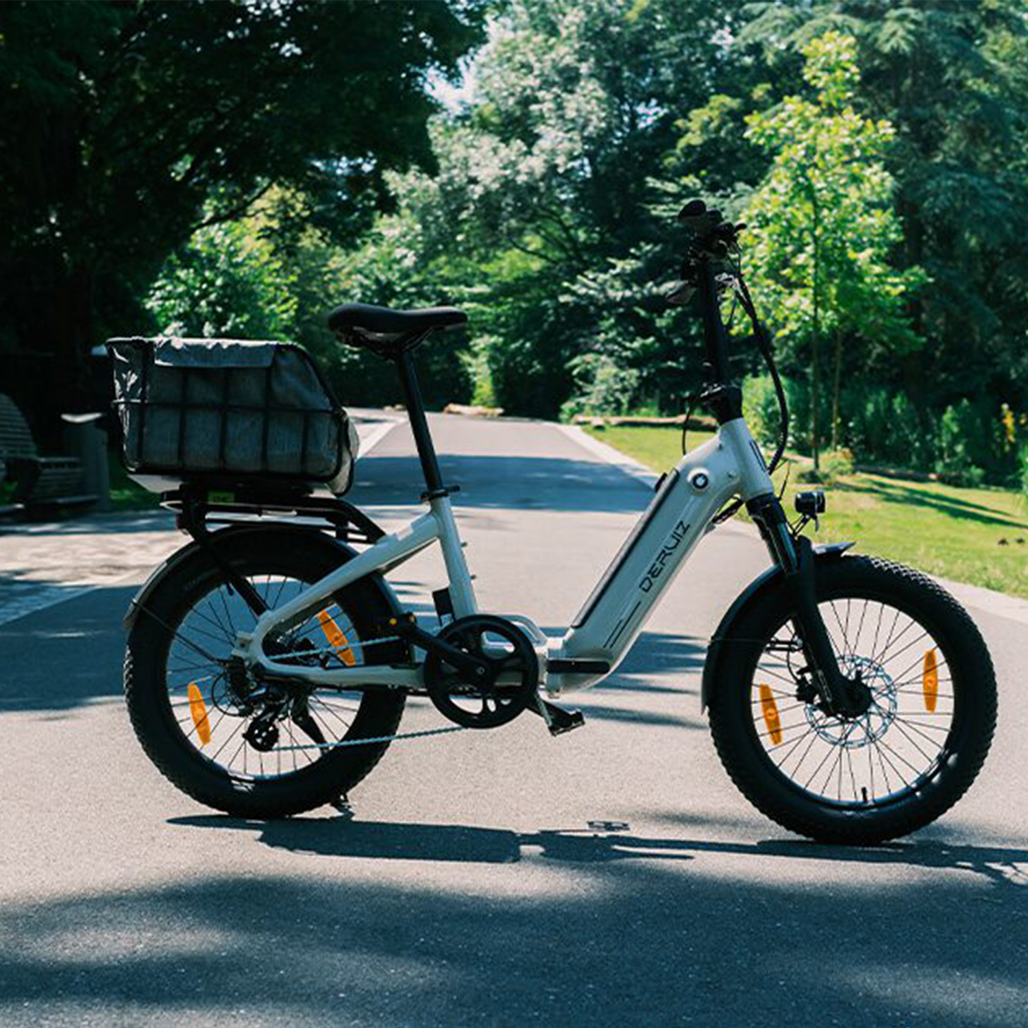 Ein weißes E-Bike mit Gepäckträger steht auf einem asphaltierten Weg im Grünen.