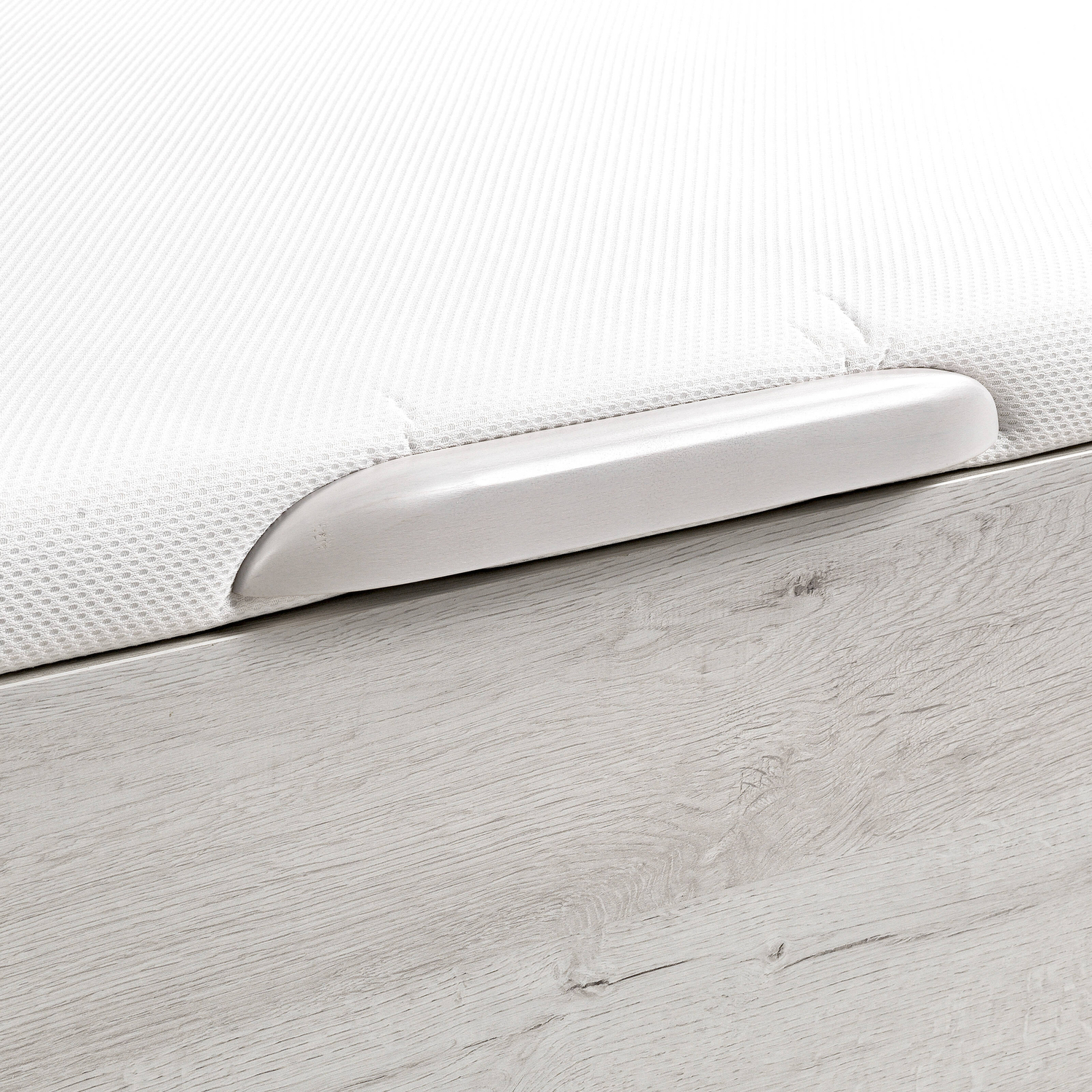 Un colchón blanco con una tira de asa plateada sobre una base de madera.