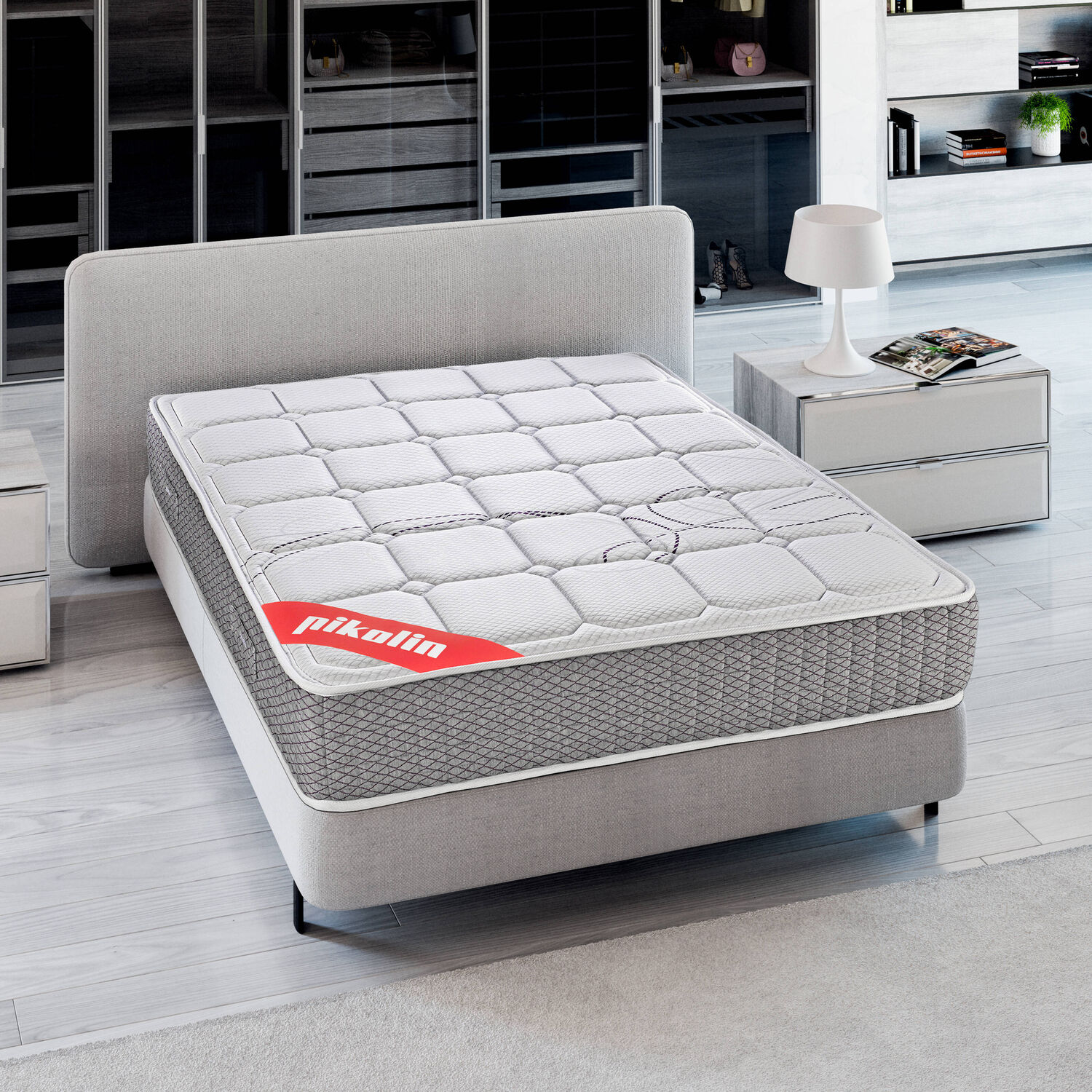 Una cama blanca y gris con colchón y una mesita de noche con lámpara.
