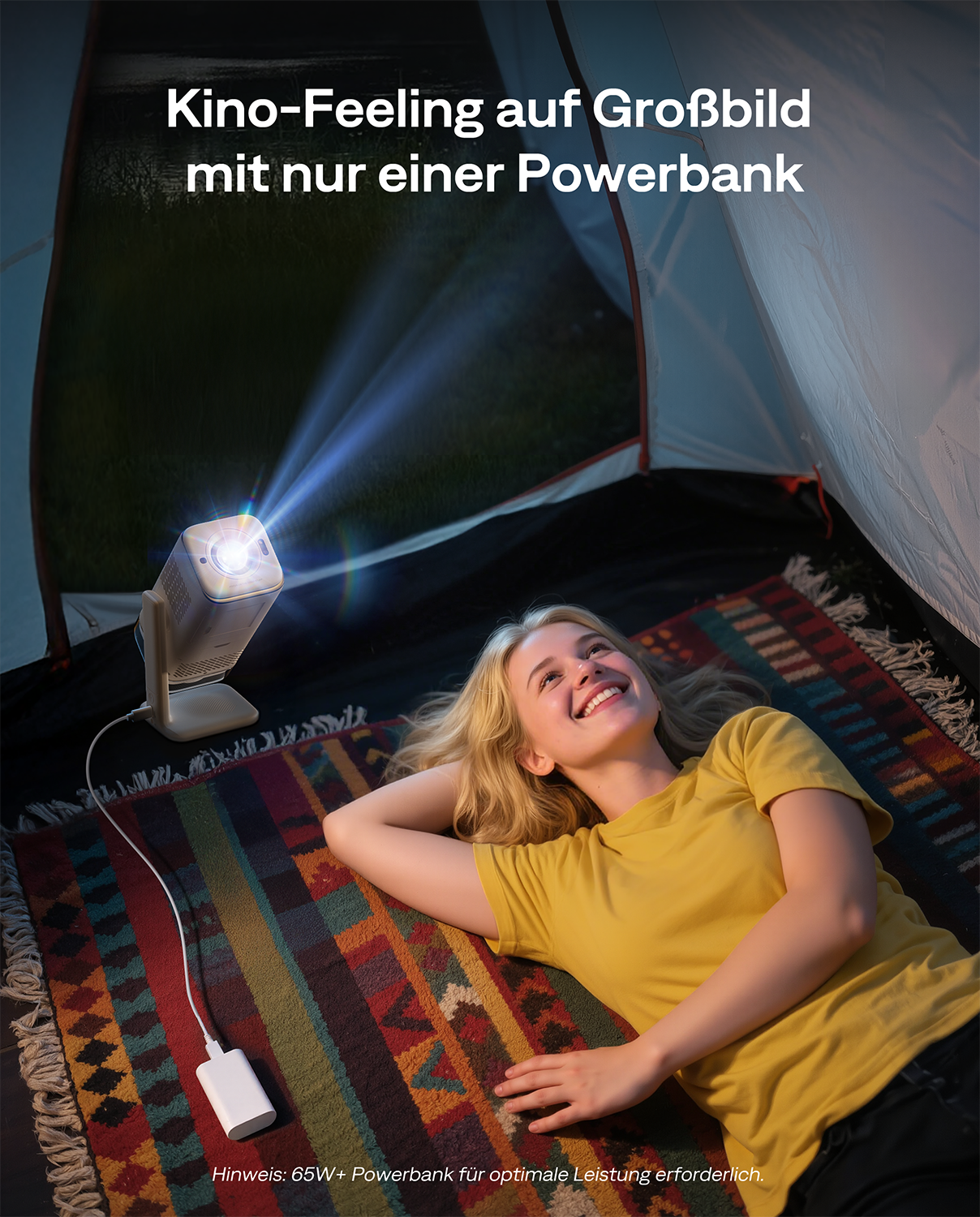 Frau liegt auf buntem Teppich in einem Zelt. Ein Projektor wirft Licht, verbunden mit Powerbank.