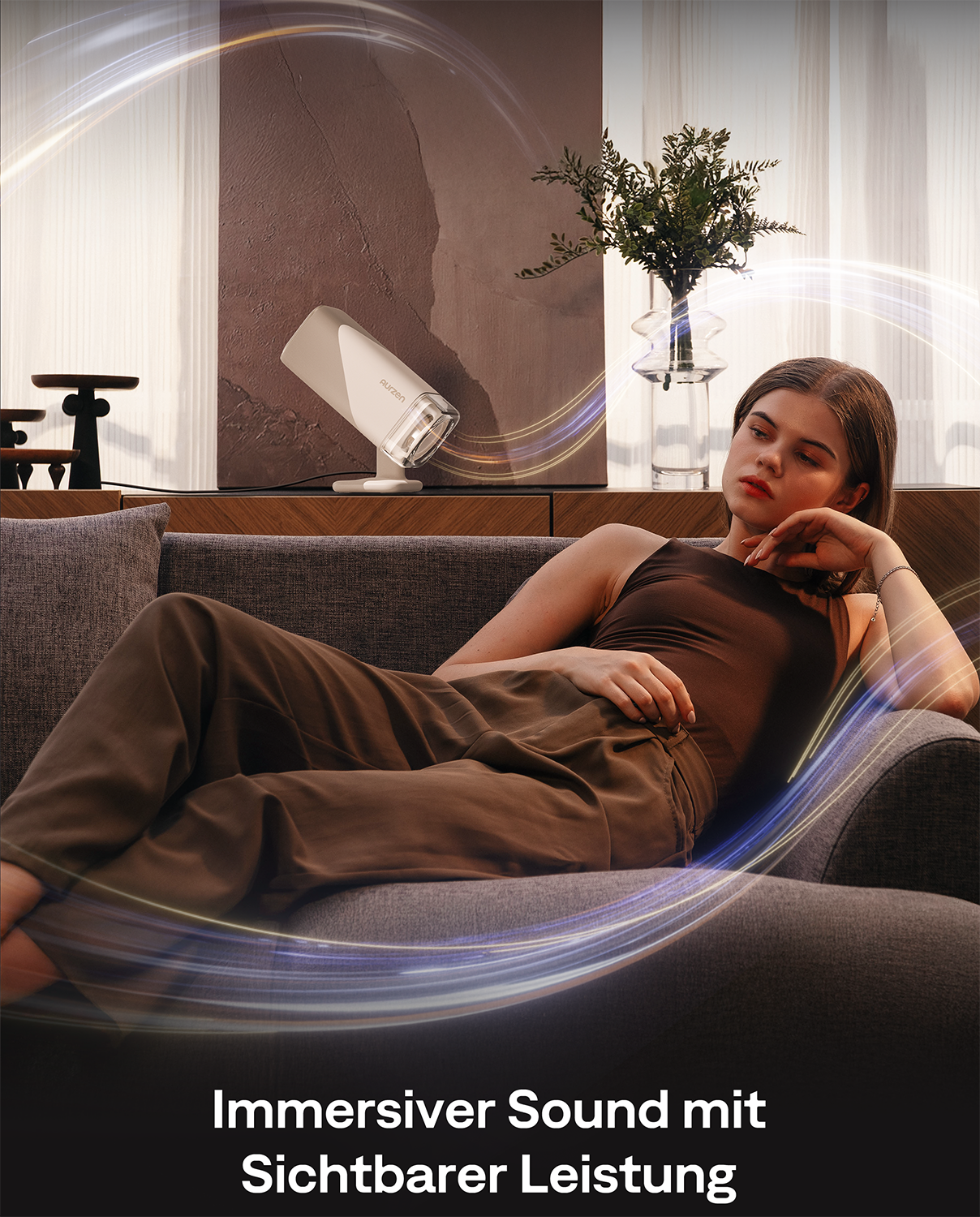 Eine Frau liegt auf einem Sofa, ein Lautsprecher steht auf einem Regal.