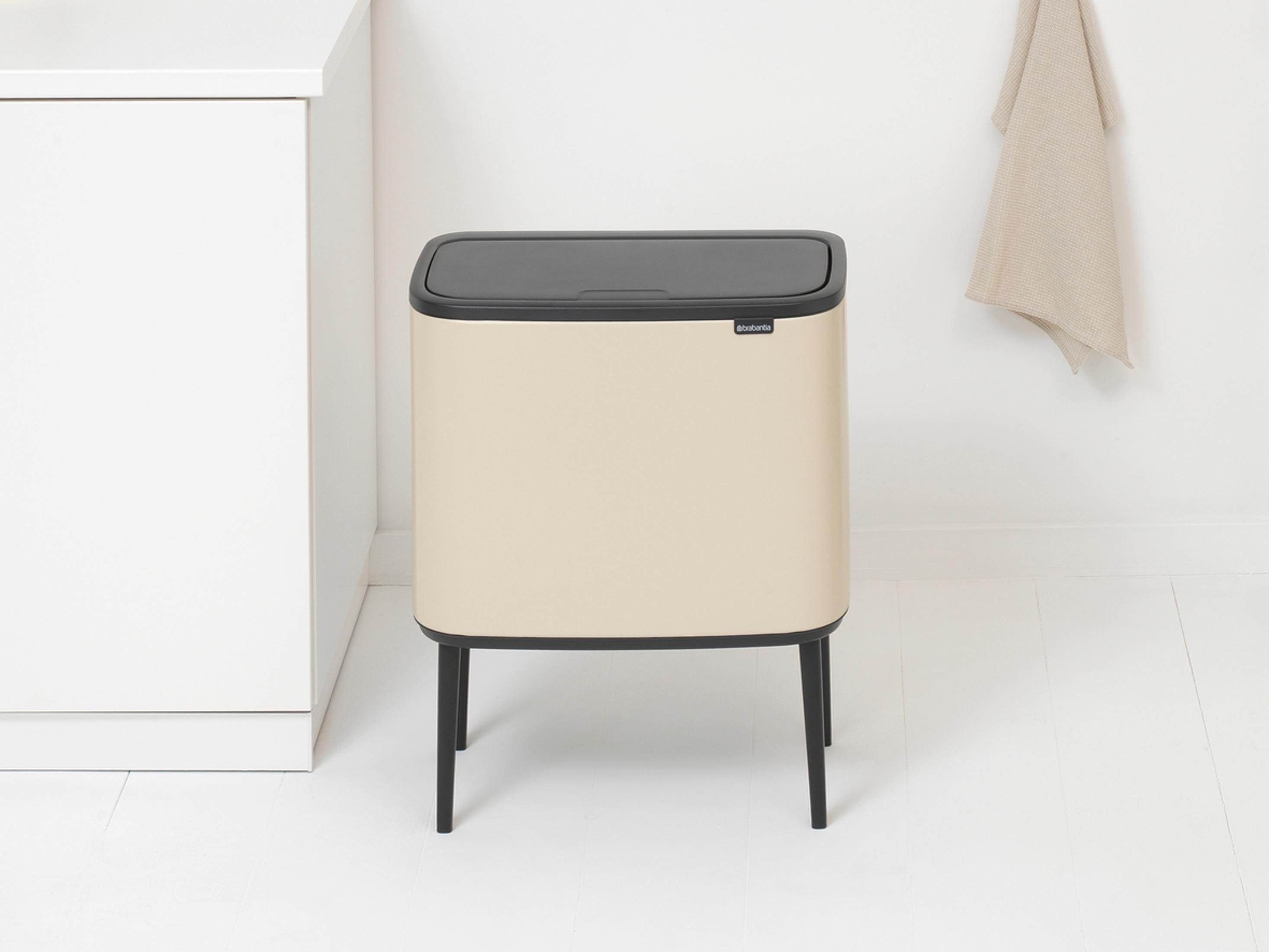 A beige bin with a black lid stands on black legs next to a white cabinet.