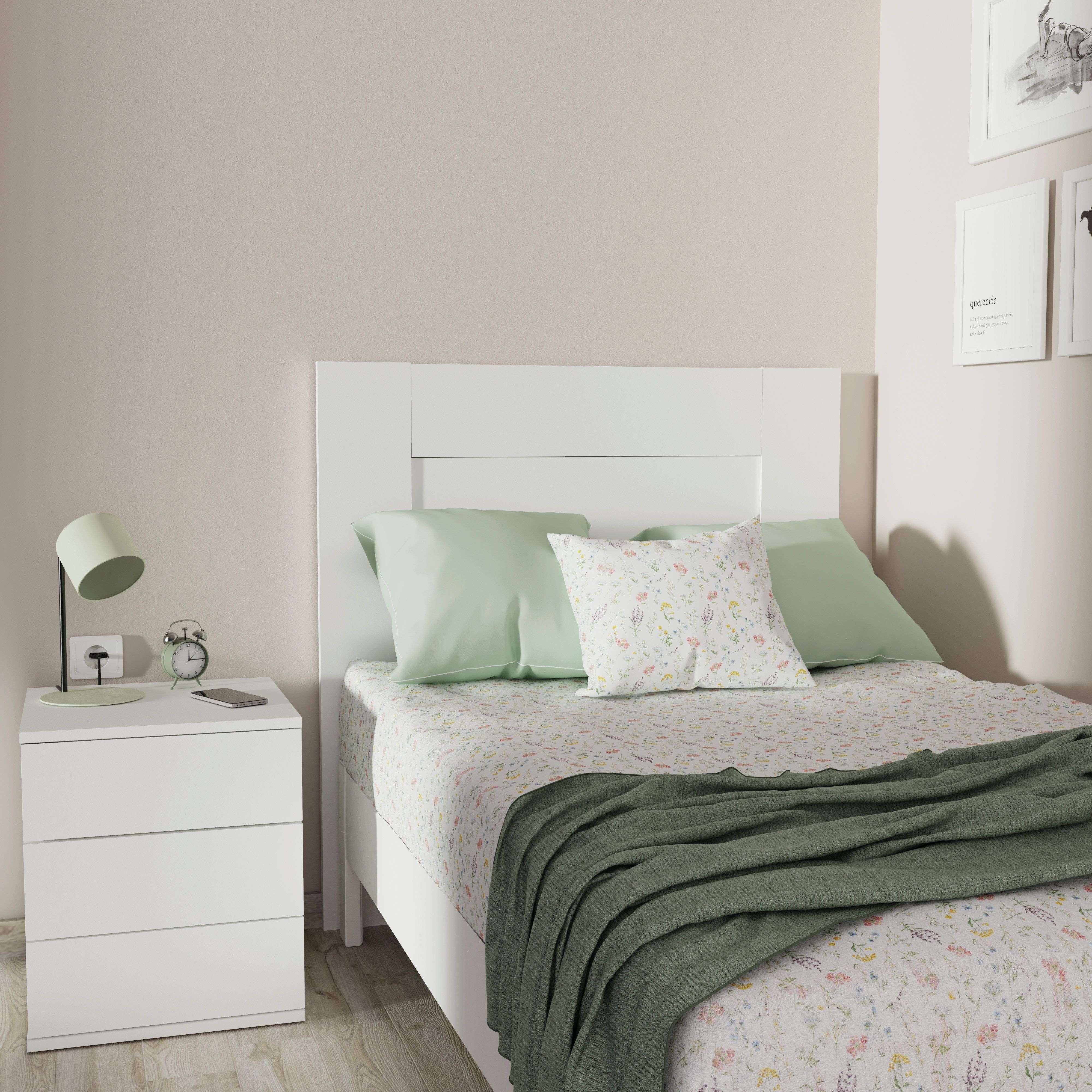 Una cama blanca con sábanas florales, almohadas verdes y manta.