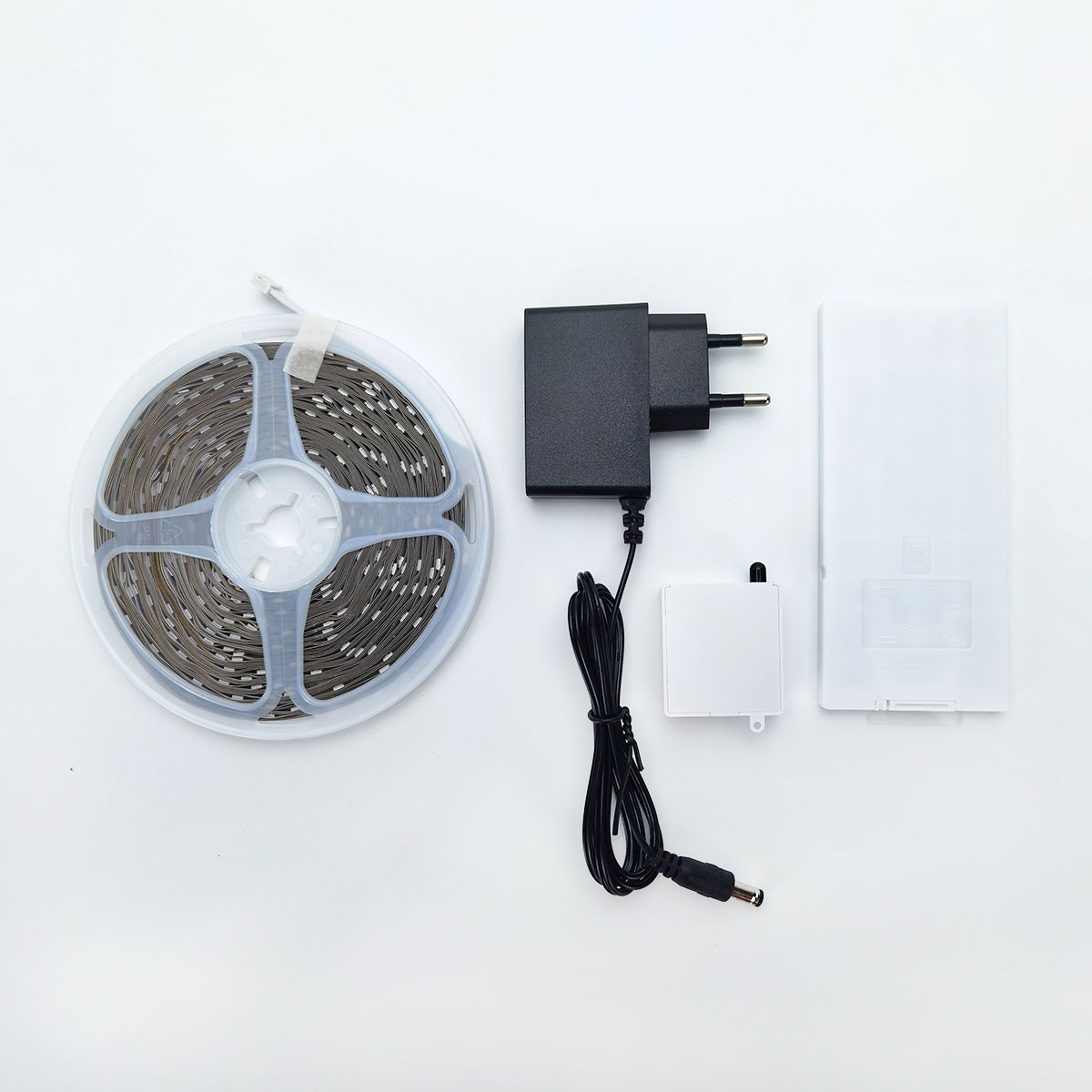 A rolled LED strip light, a black power adapter, a small white box, and a white case.