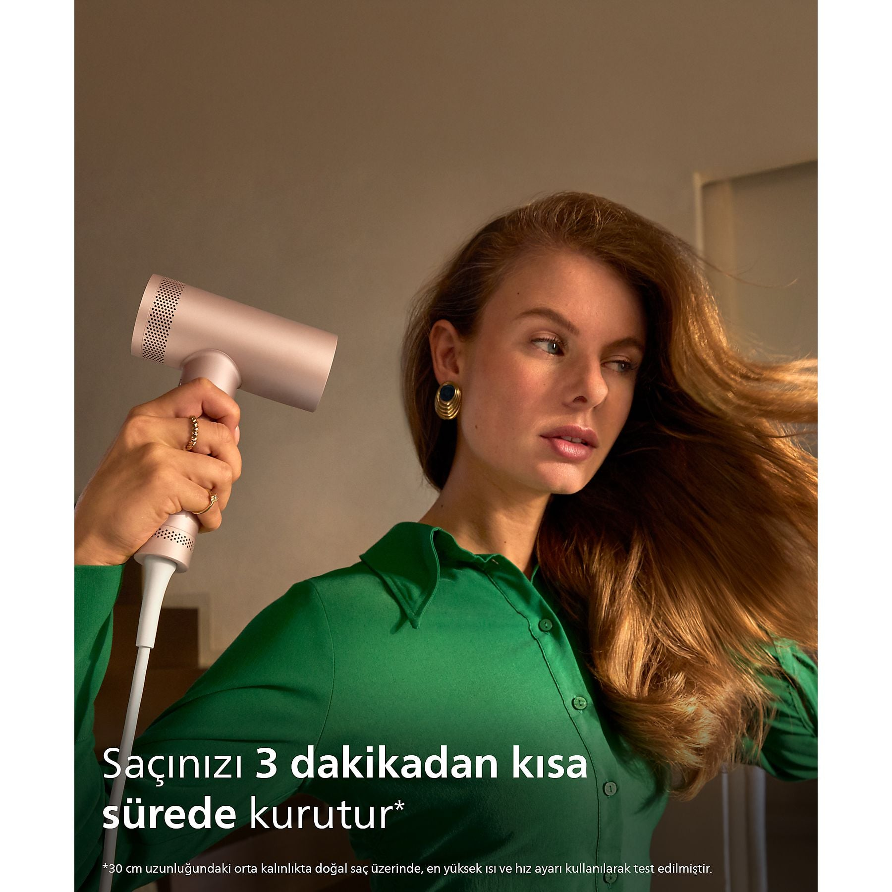 Mujer con secador rosa dorado y camisa verde, su pelo ondea.