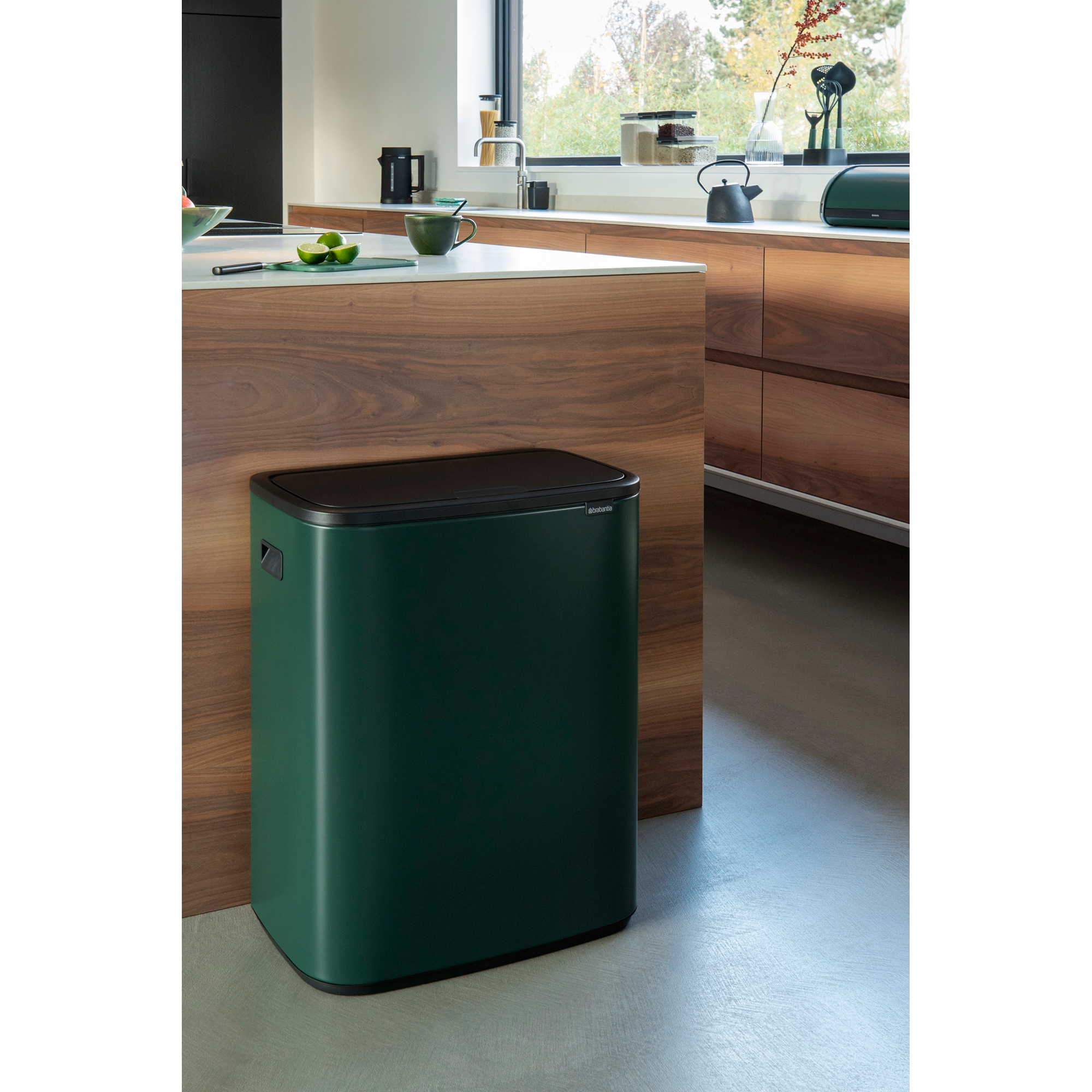 Donkergroene prullenbak met zwart deksel naast een houten aanrecht in een moderne keuken.