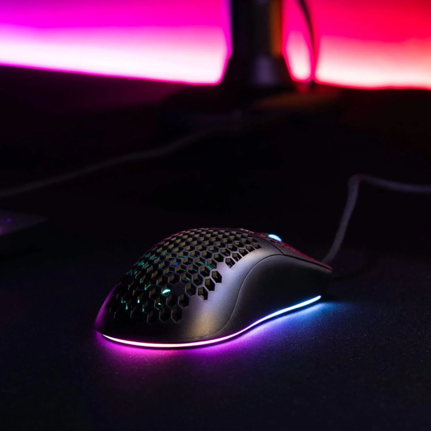 Black honeycomb gaming mouse with RGB lighting on a dark surface.